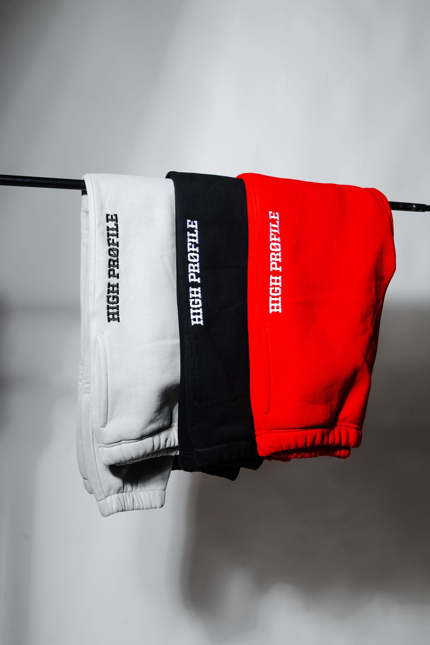 Three sweatpants in white, black, and red hanging on display against gray wall.