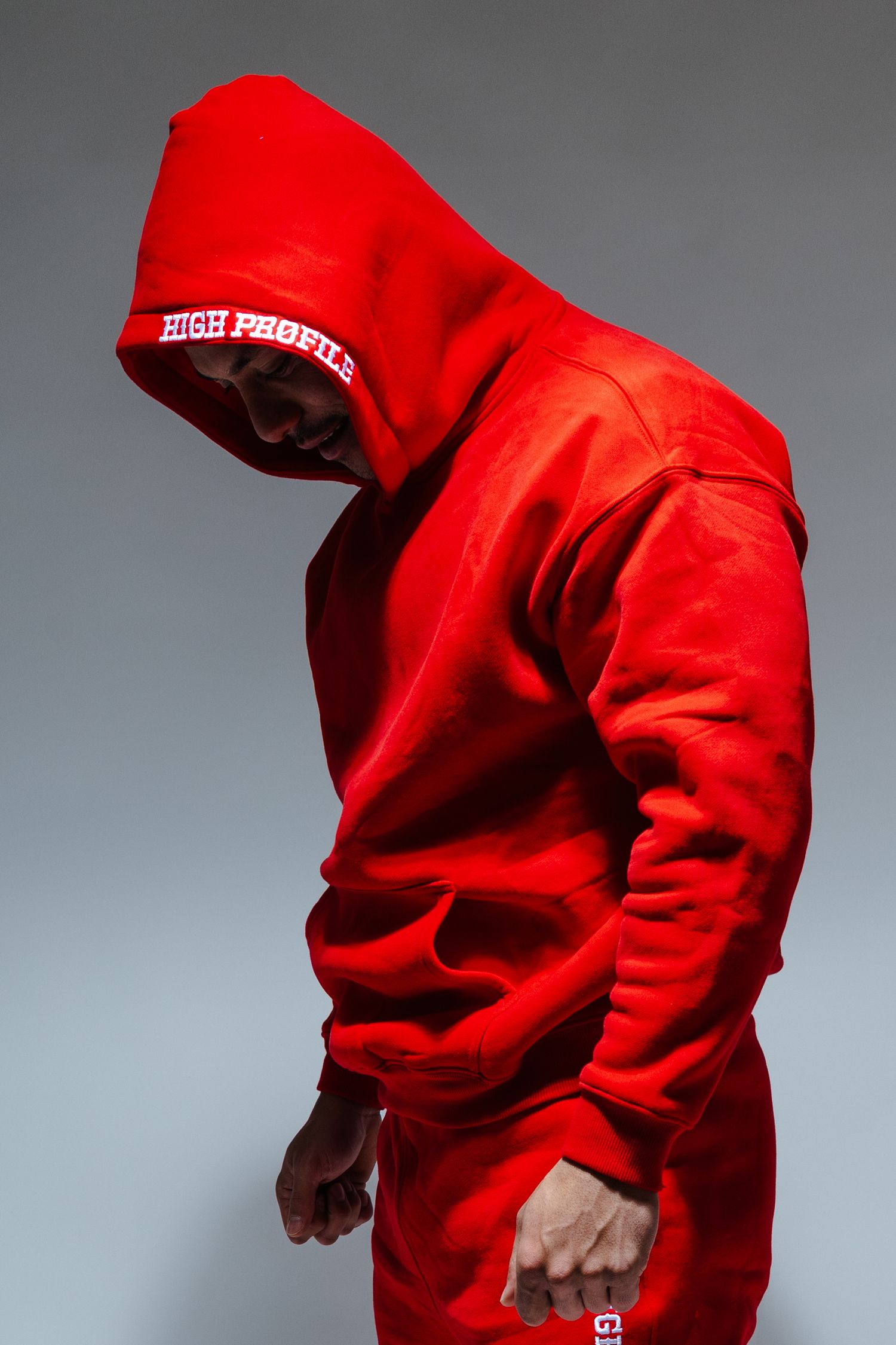 Person wearing a bright red hoodie tracksuit posing against a grey background in dramatic lighting.