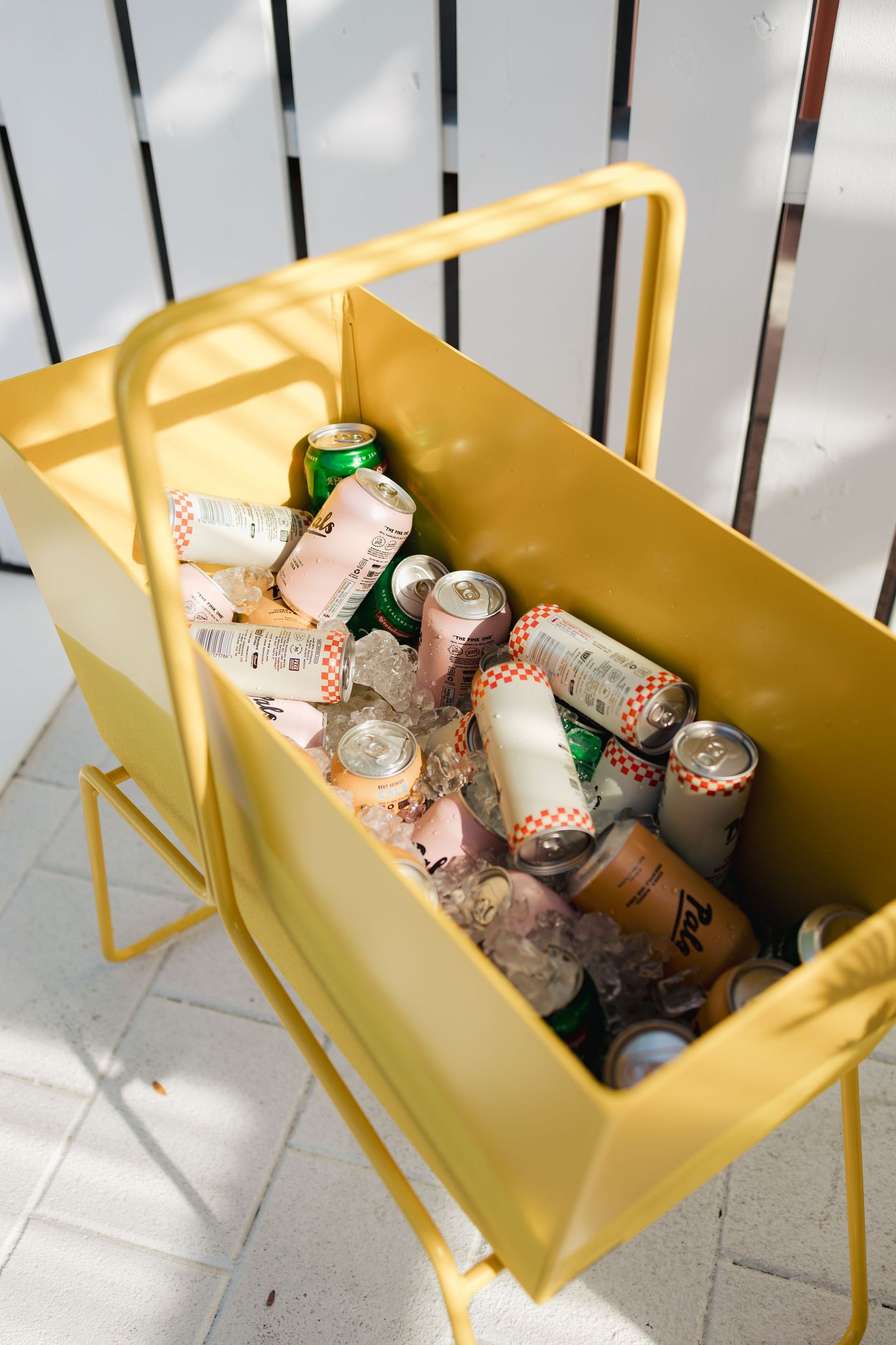 Yellow metal beverage cart filled with canned drinks on white patio.