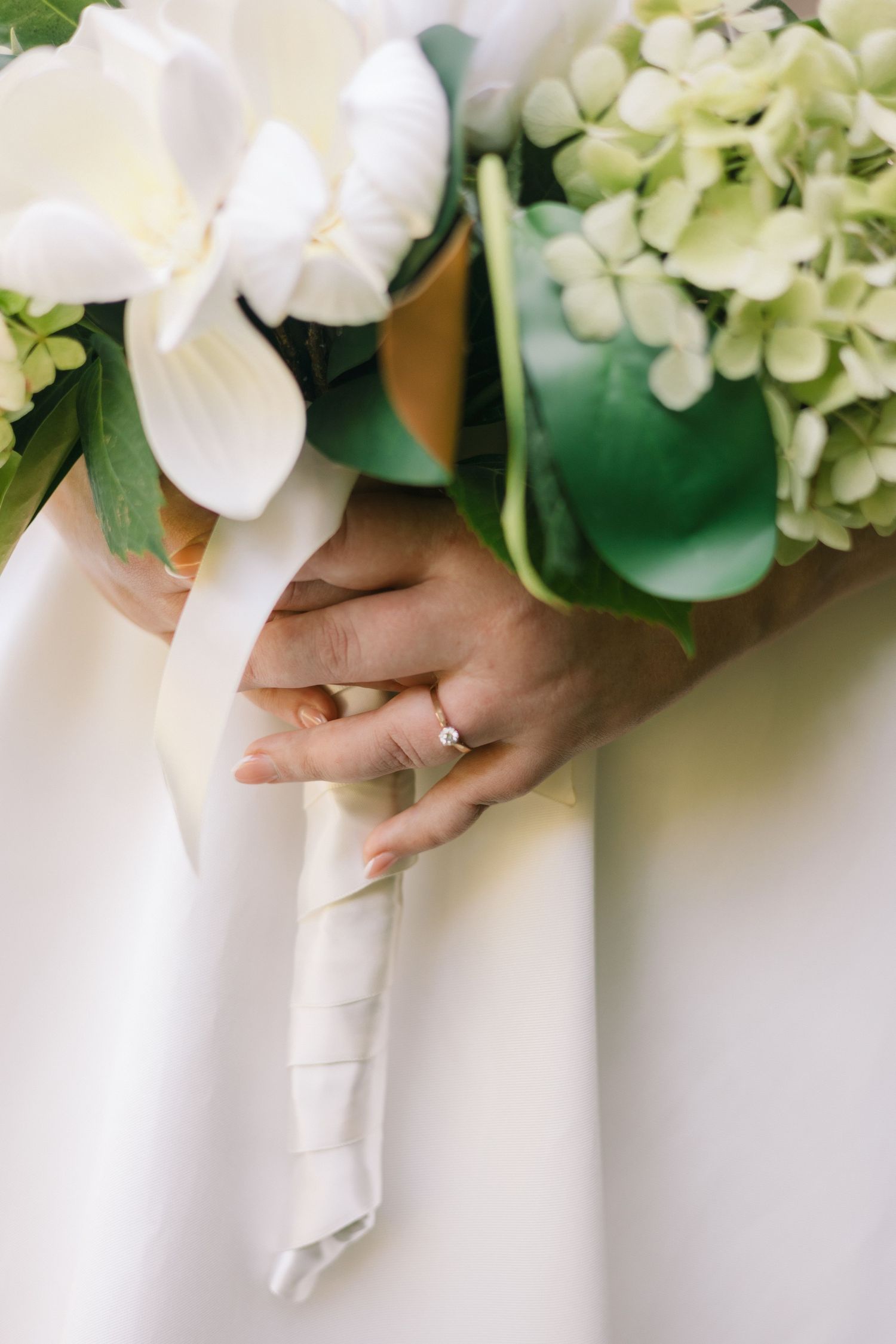 Close-up of wedding bouquet with white orchids and hydrangeas alongside bride's hand showing wedding ring.