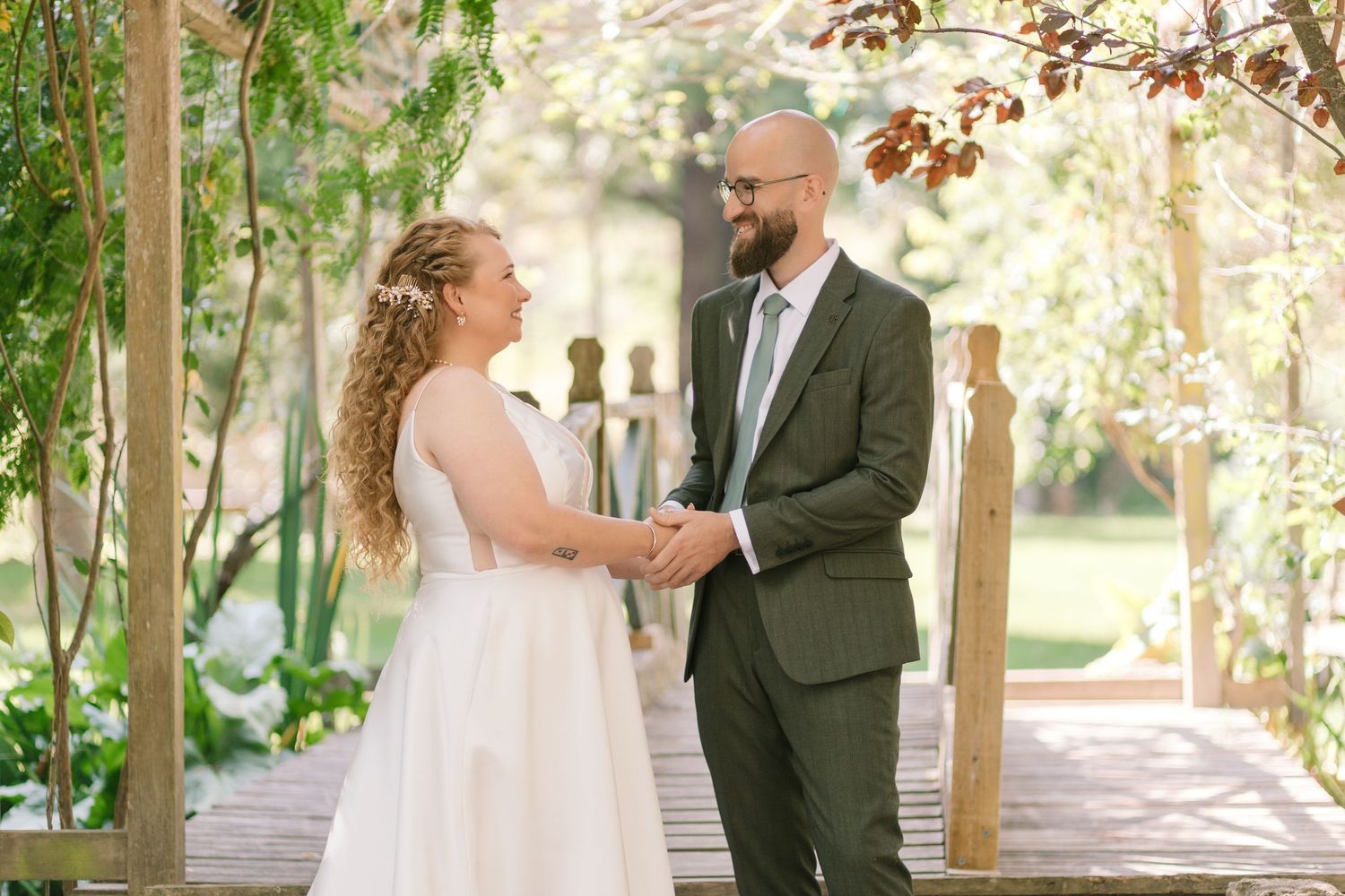 A couple shares a tender moment on a wooden bridge during their wedding ceremony surrounded by greenery.