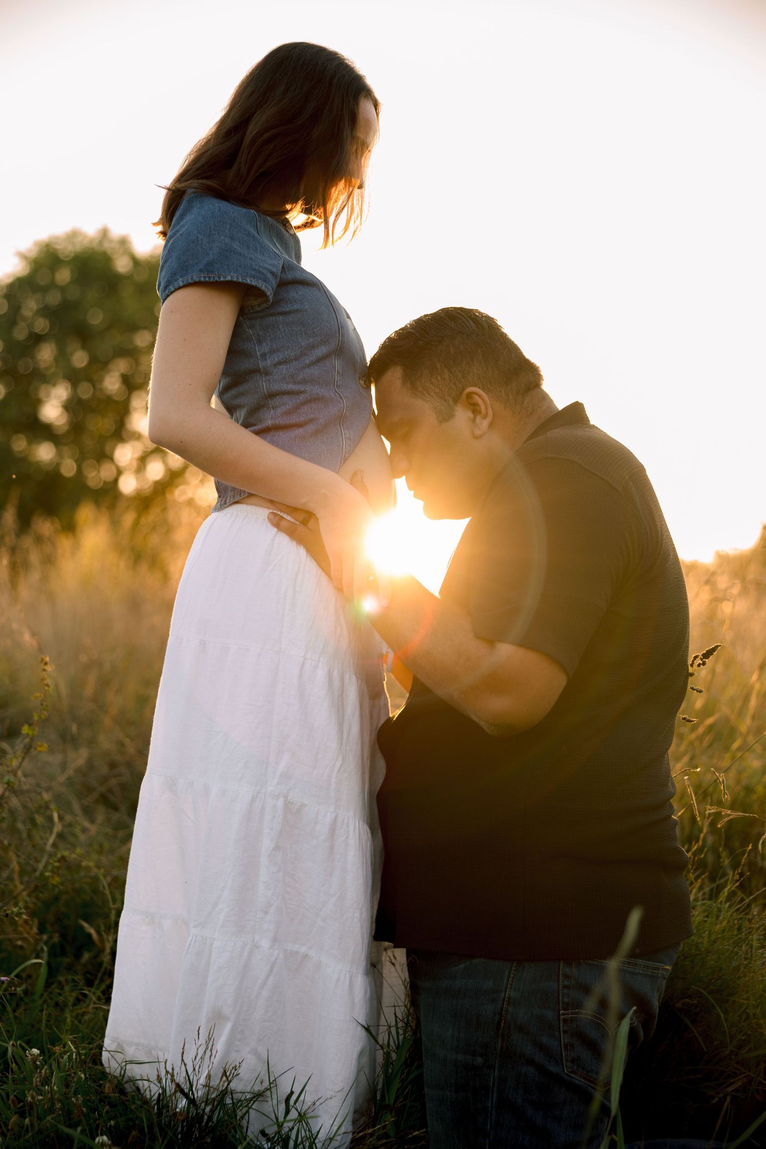 Romantic silhouette of a couple embracing in a sunlit meadow at golden hour, with sun flare creating a dreamy atmosphere.