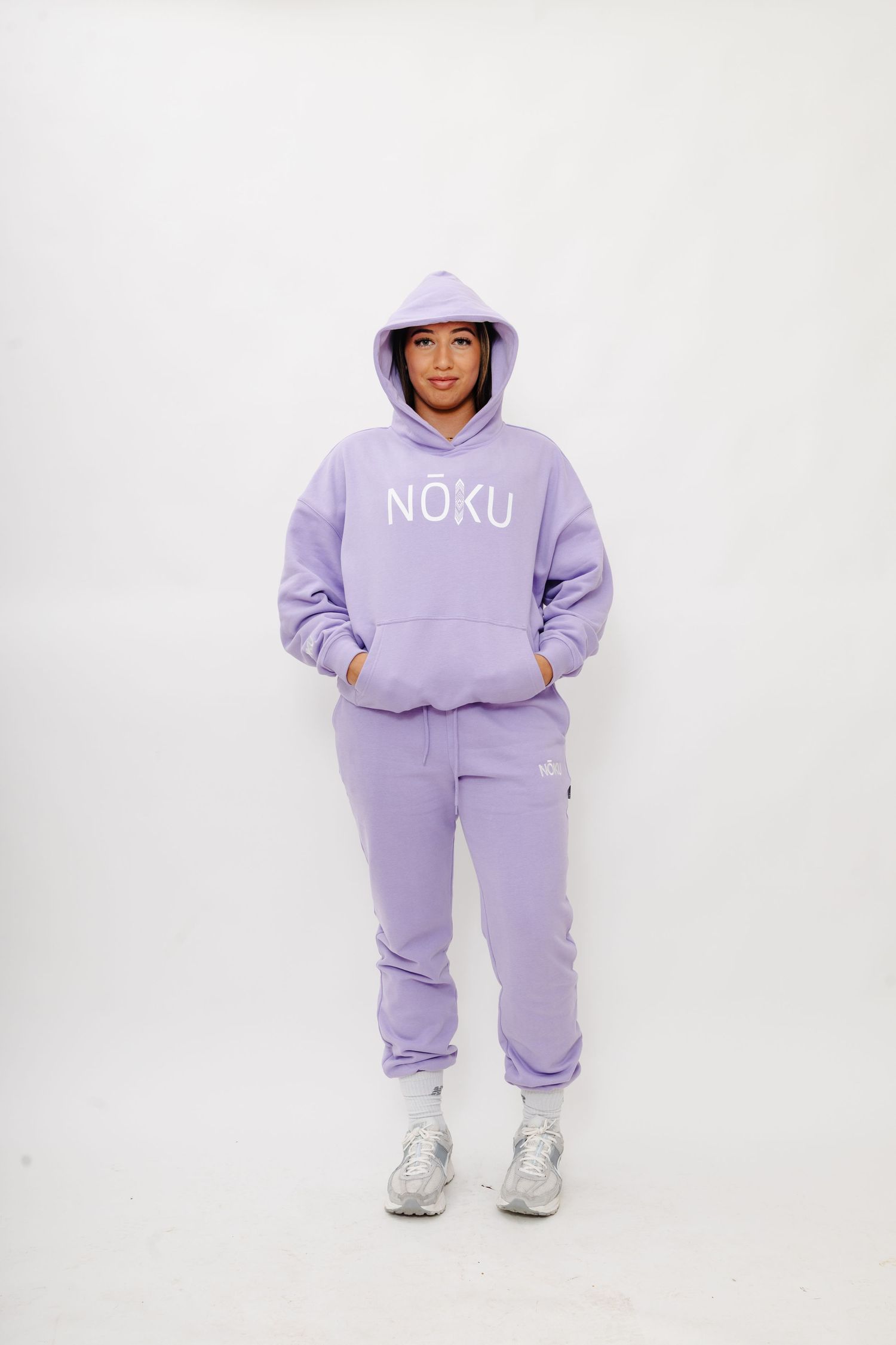 A person wearing a cozy lilac sweatsuit and white sneakers poses against a white background.