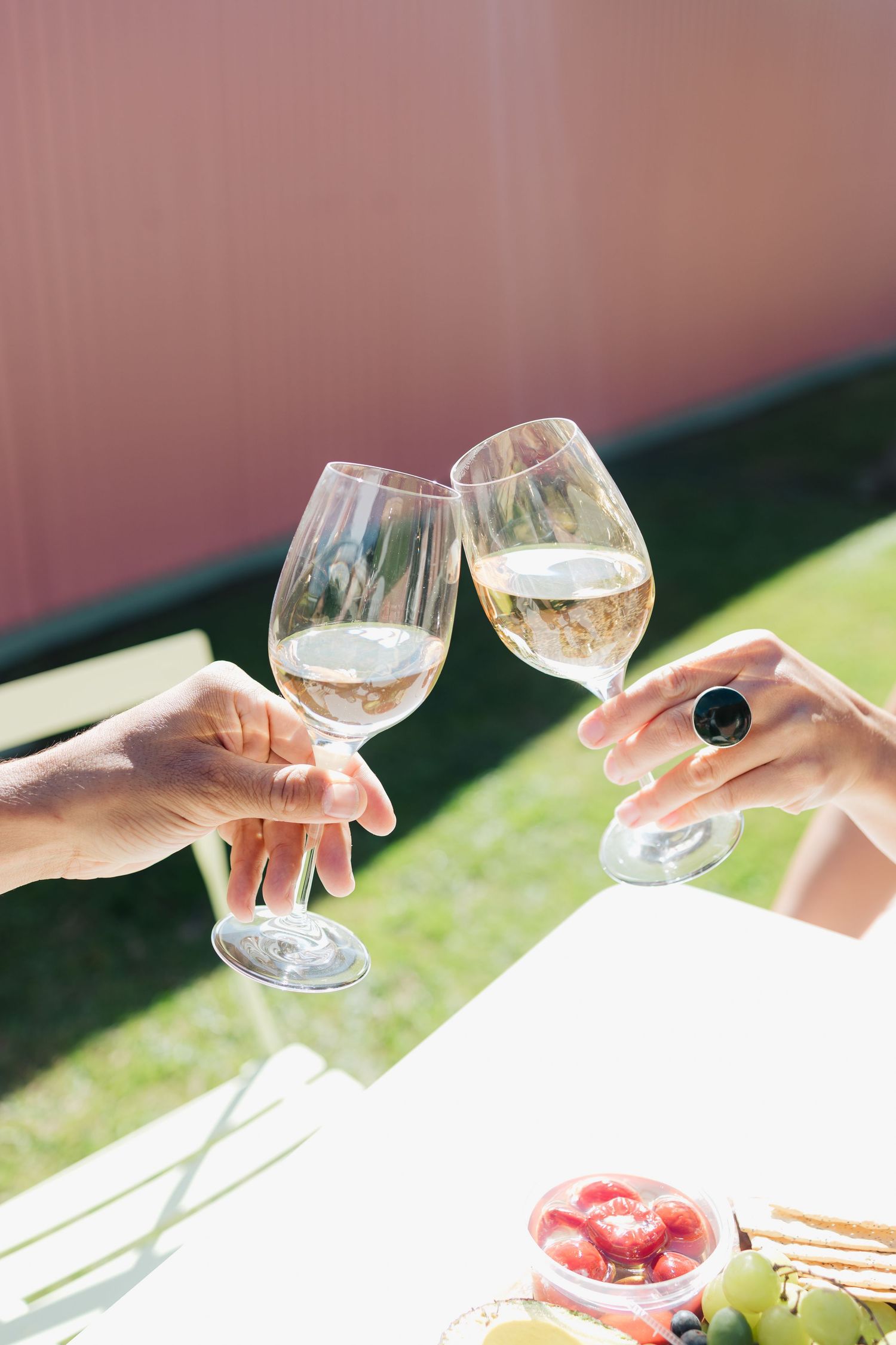 Two wine glasses clinking in sunlight over an outdoor table setting.