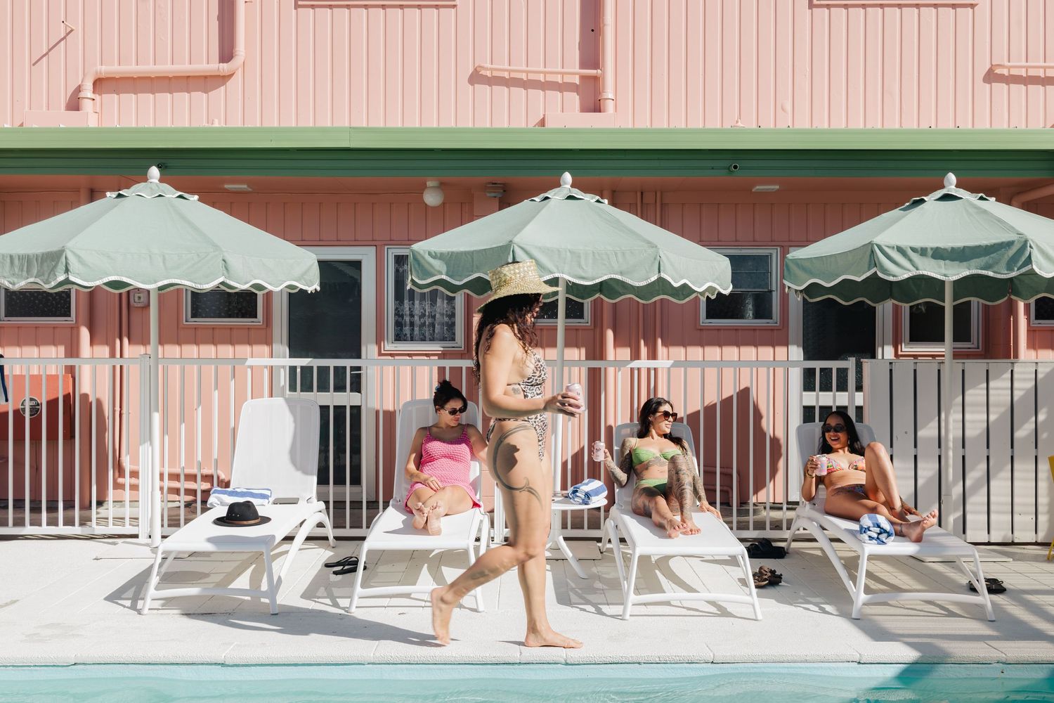People relaxing on lounge chairs by pool with mint green umbrellas.