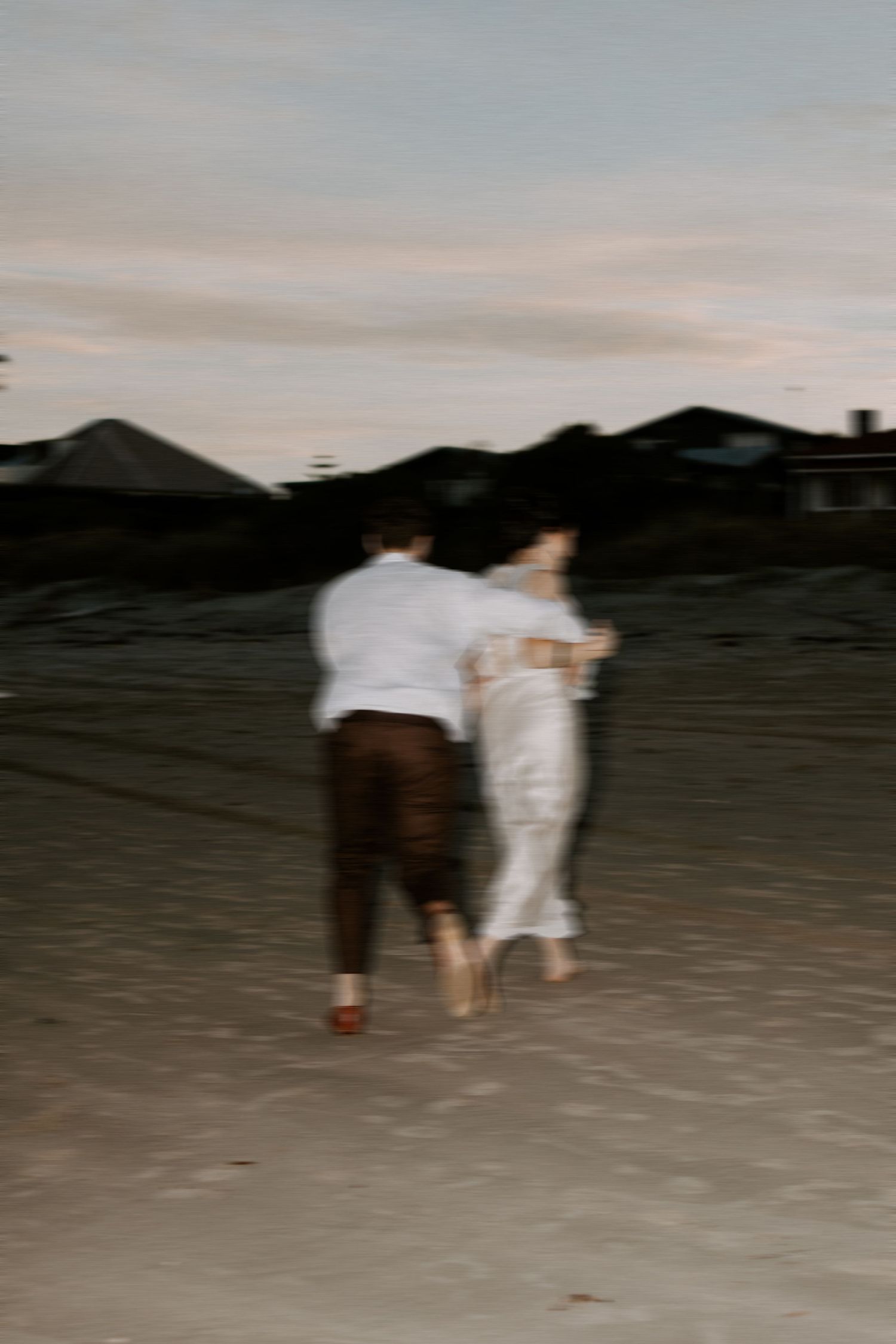 Blurred silhouettes walking on sandy beach at dusk with mountain backdrop.