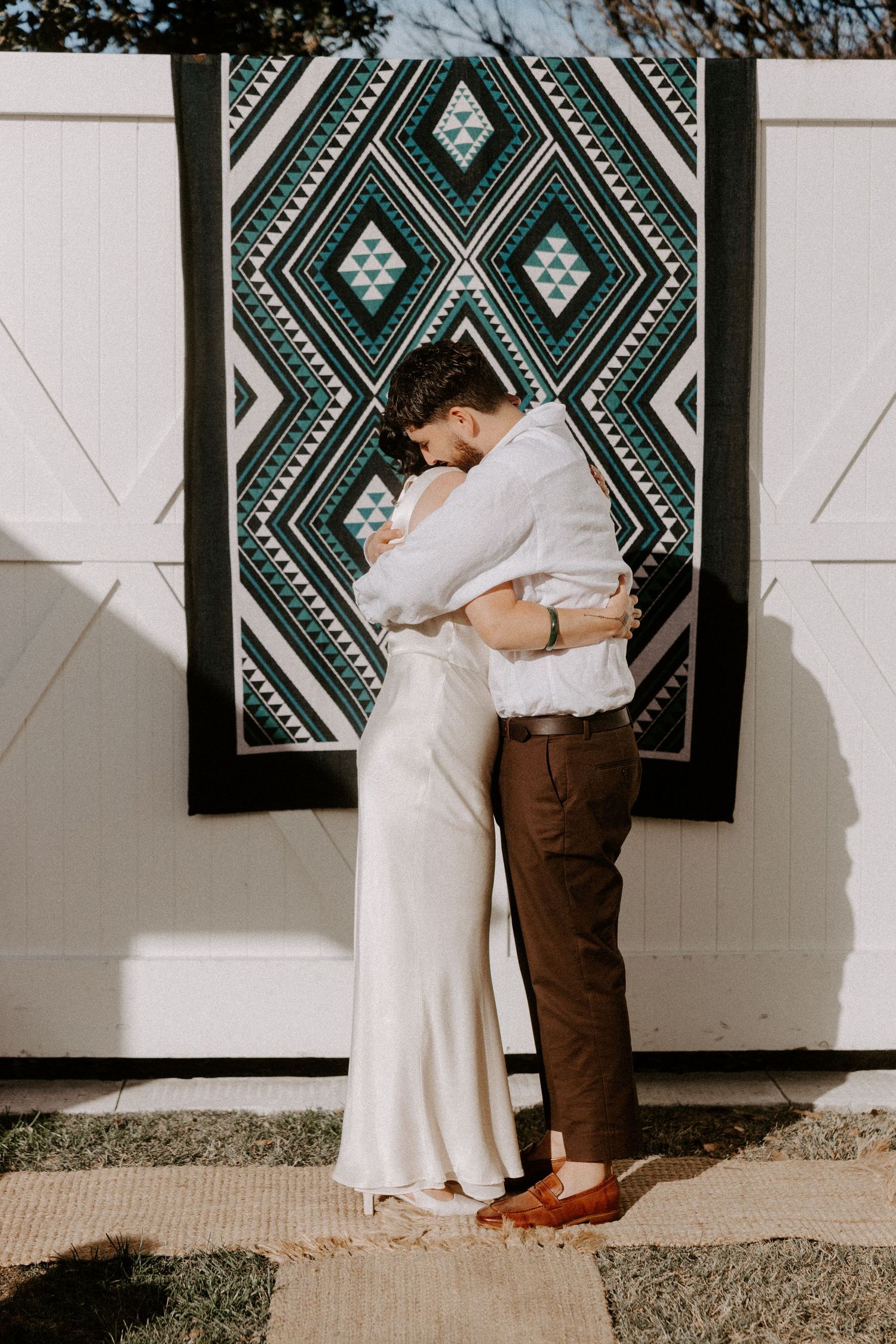 Couple embracing outdoors against a decorative green and white geometric patterned wall.