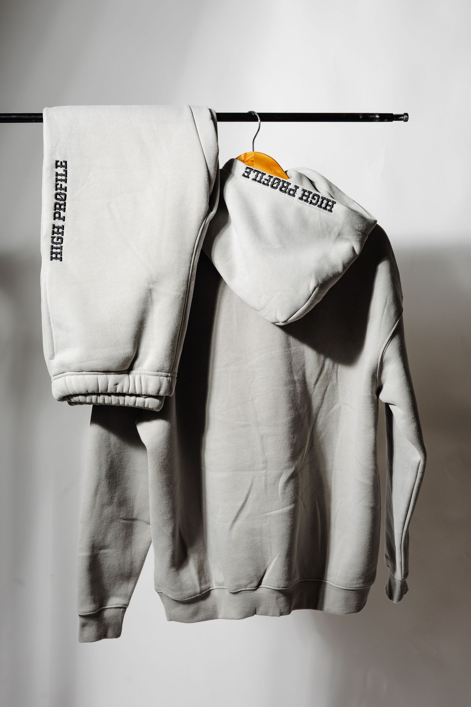 White sweatsuit set hanging on wooden hanger against neutral background.