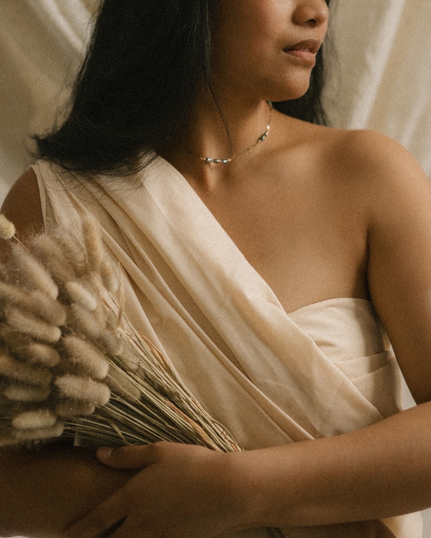 Artistic portrait in sepia tones showing delicate drapery, dried wheat stems, and a minimalist moon phase necklace.