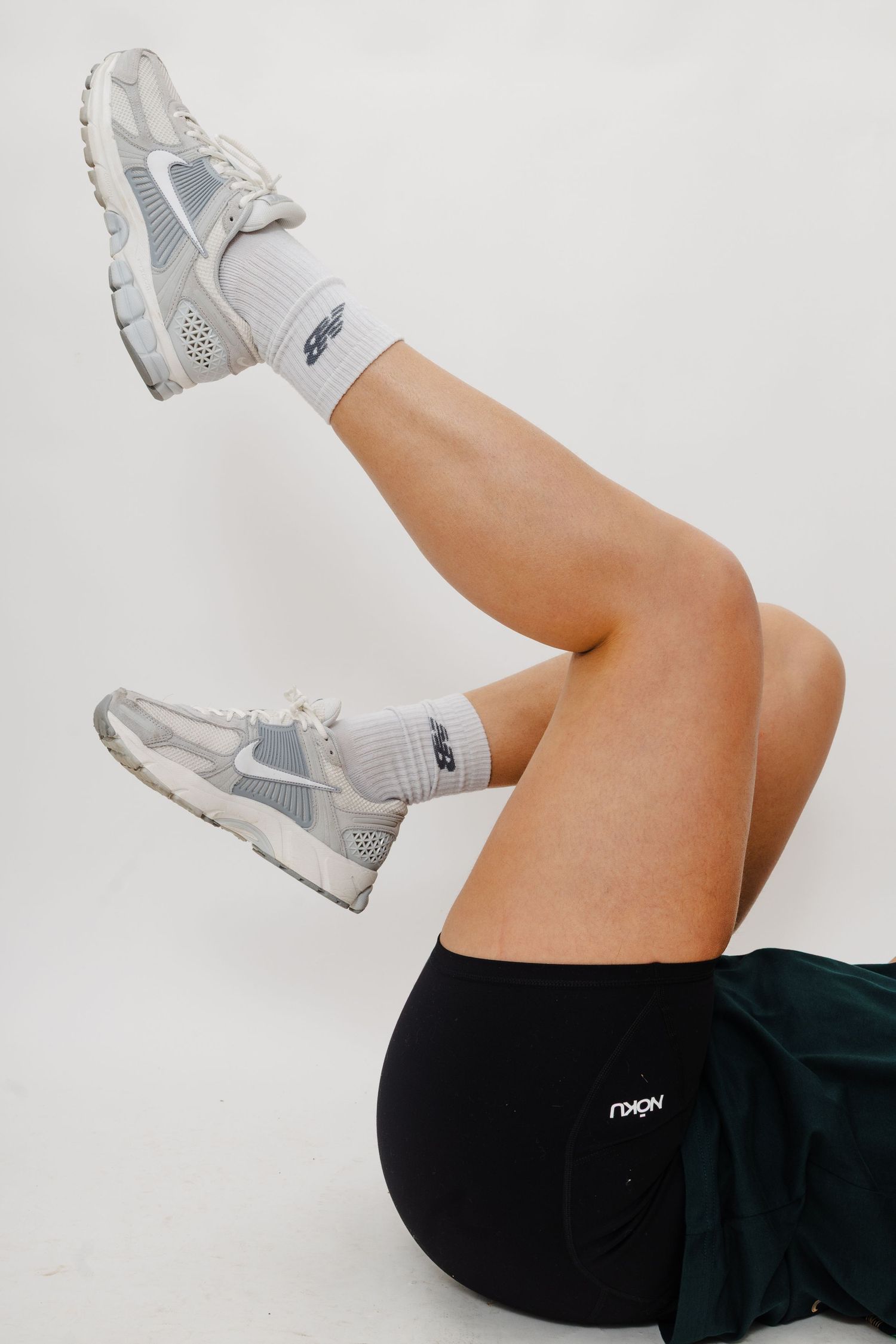 Athletic legs in white sneakers and black shorts performing dynamic leg raises against white background.