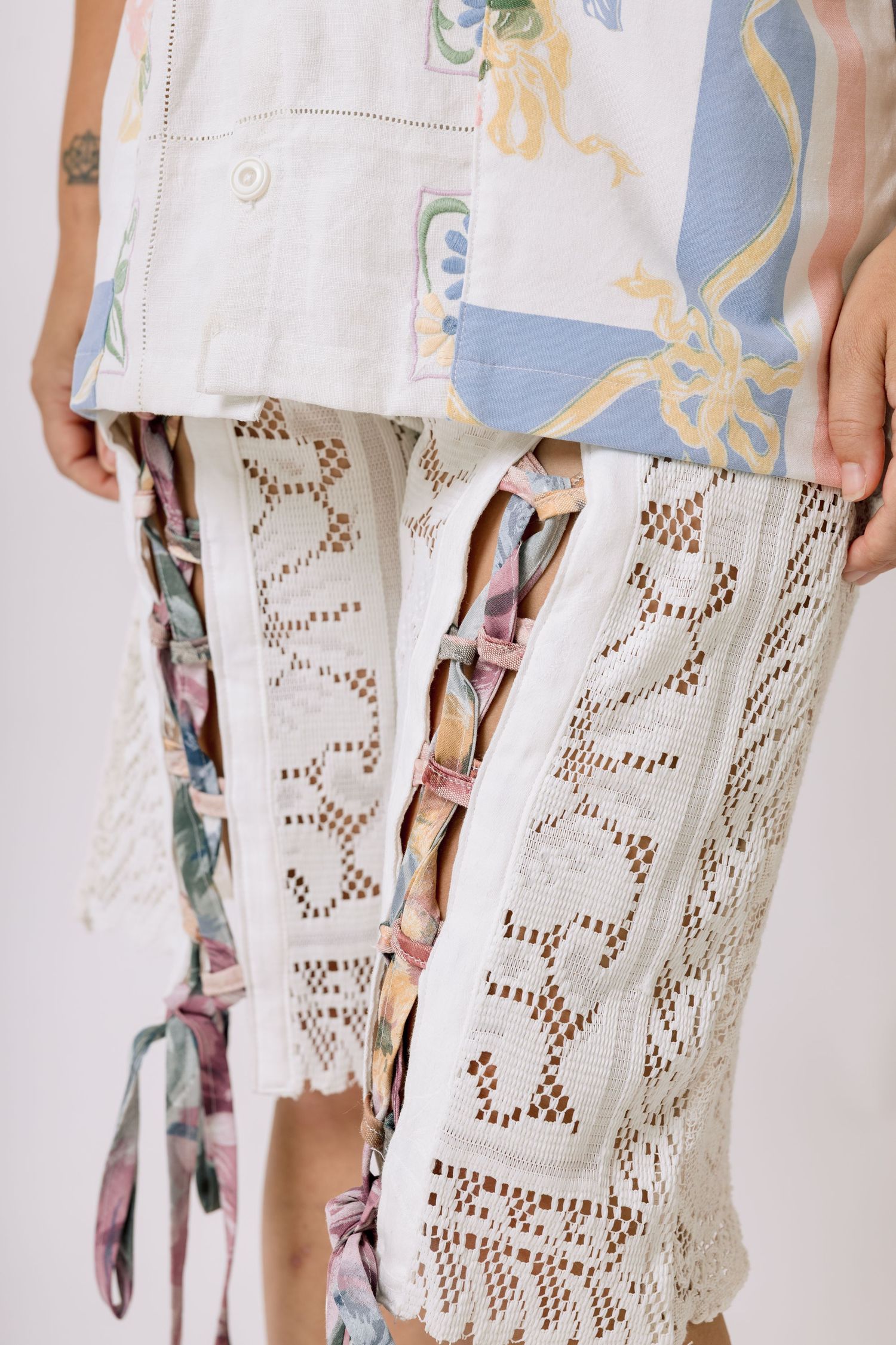 Close-up view of intricate white lace cutout pattern details on clothing fabric against a light background.