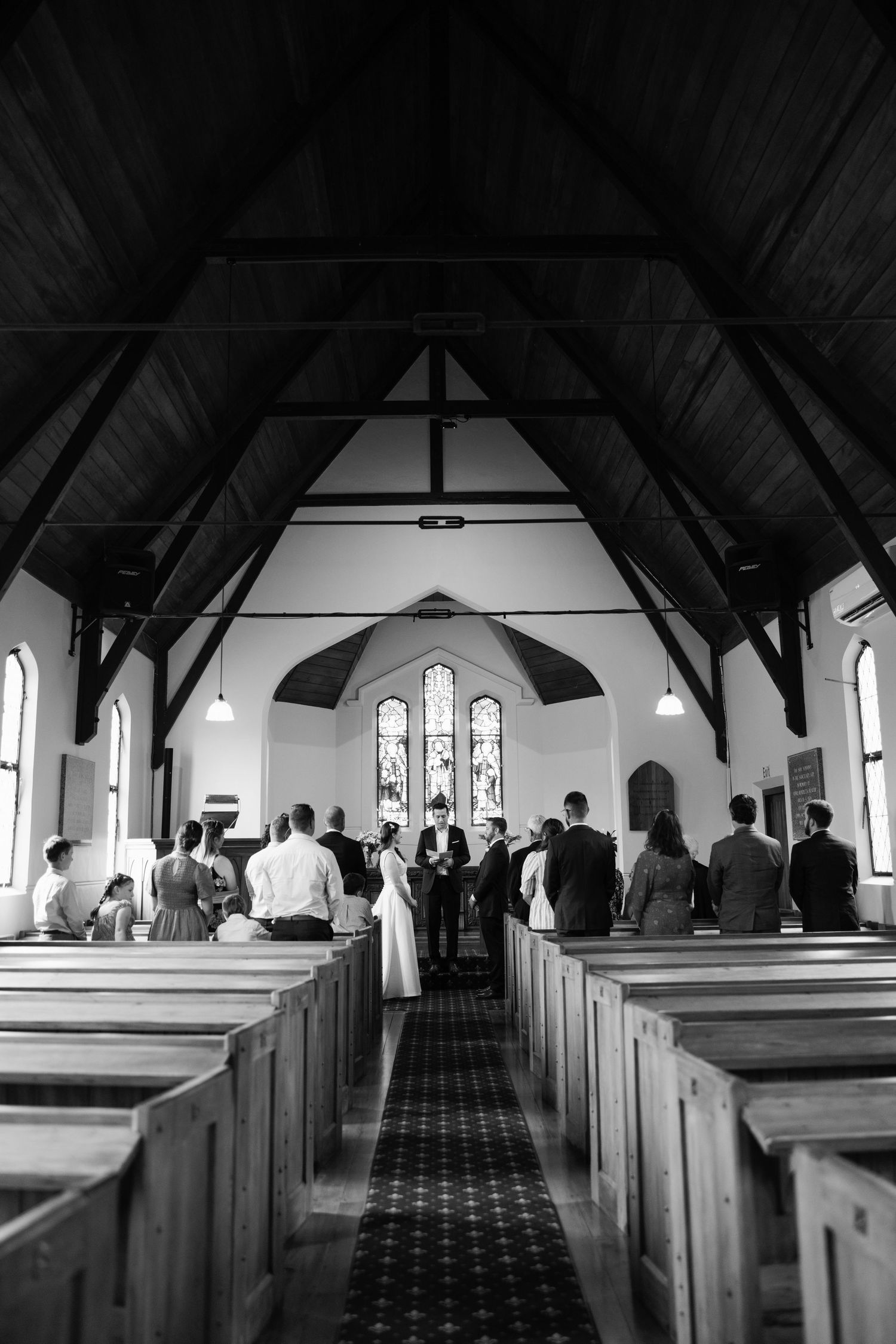 Interior view of a traditional church sanctuary with wooden pews and gothic arched windows in black and white.