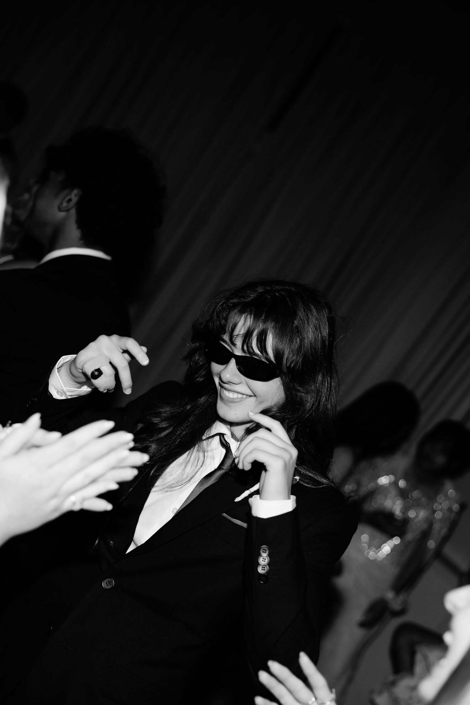 Person in sunglasses and black suit smiling while dancing at a formal event, black and white photo.