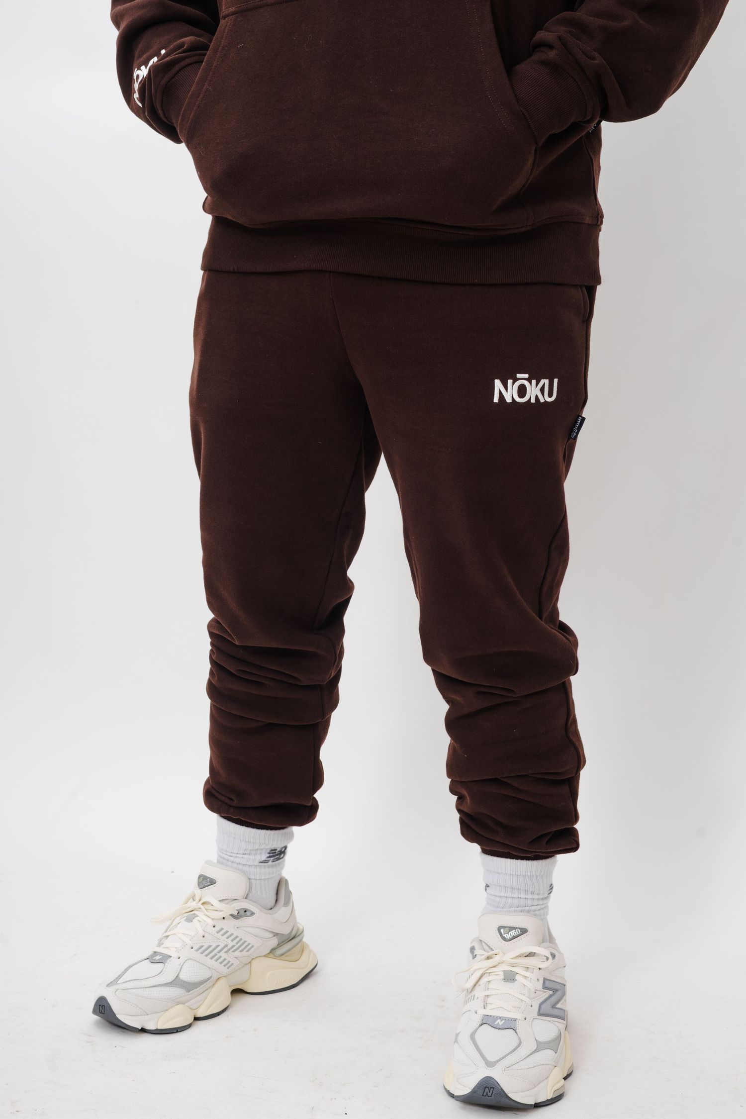 Brown sweatpants and cream-colored athletic shoes shown against a white studio backdrop.