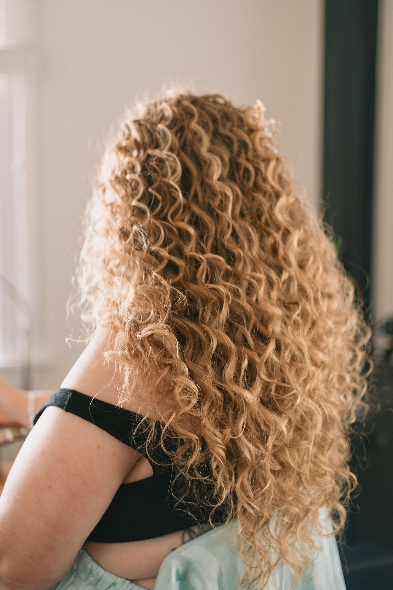 Close-up view of long, natural blonde curly hair cascading down from behind.