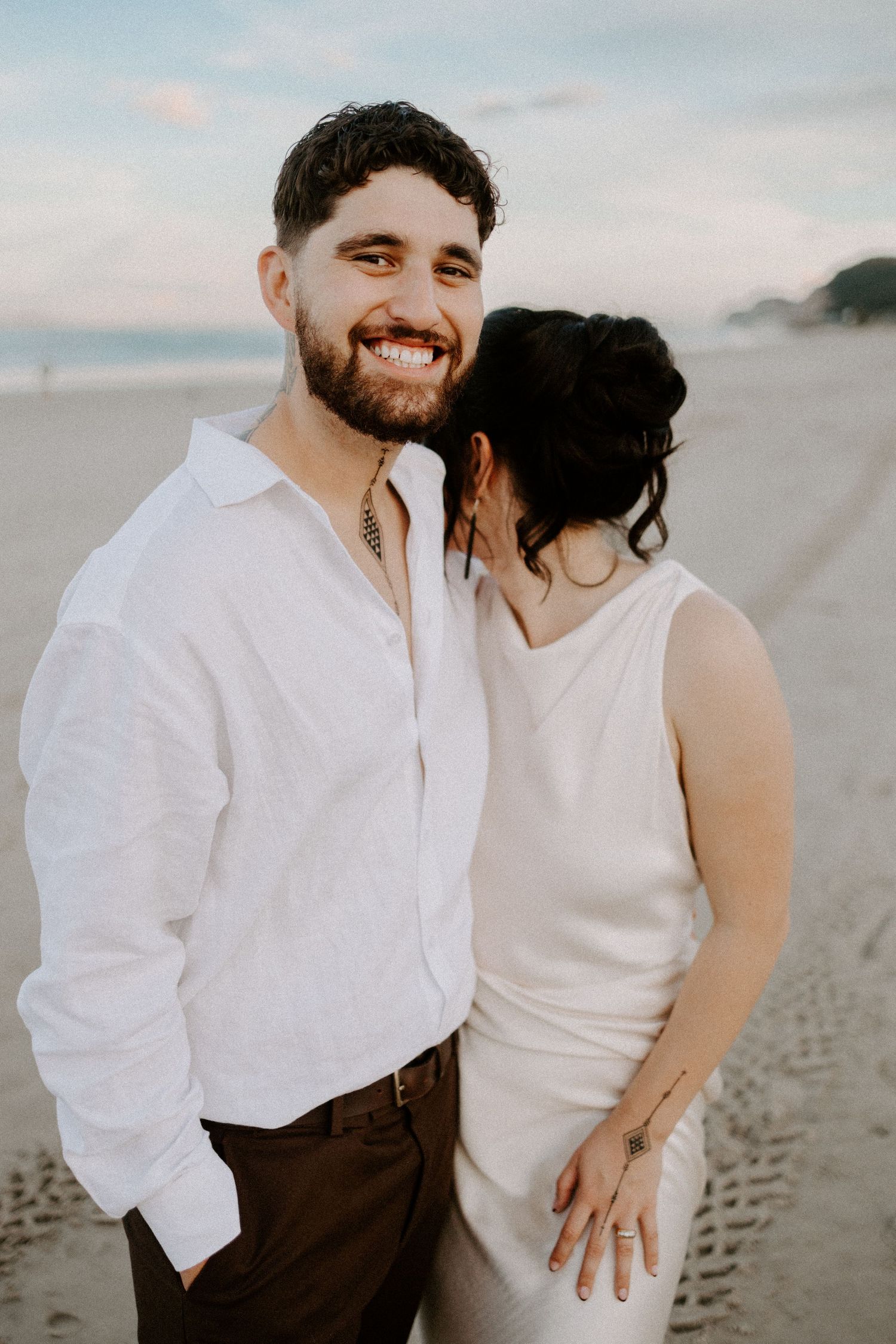 A romantic beach wedding portrait at sunset with soft pastel skies.