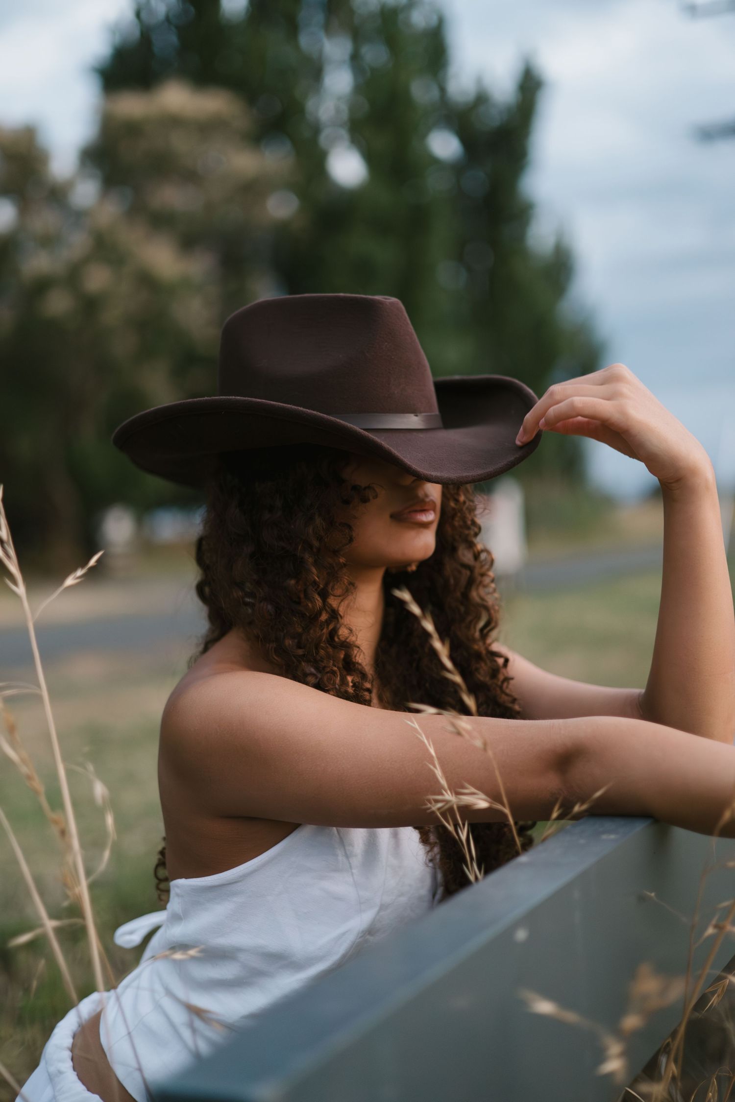 Person in brown cowboy hat and white top gazes into distance against blurred outdoor landscape.