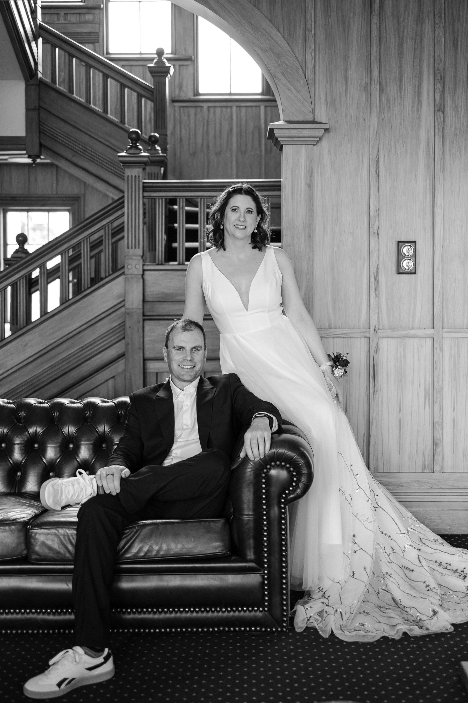 Wedding portraits on a leather couch showing the bride's dress and groom's formal attire in black and white.