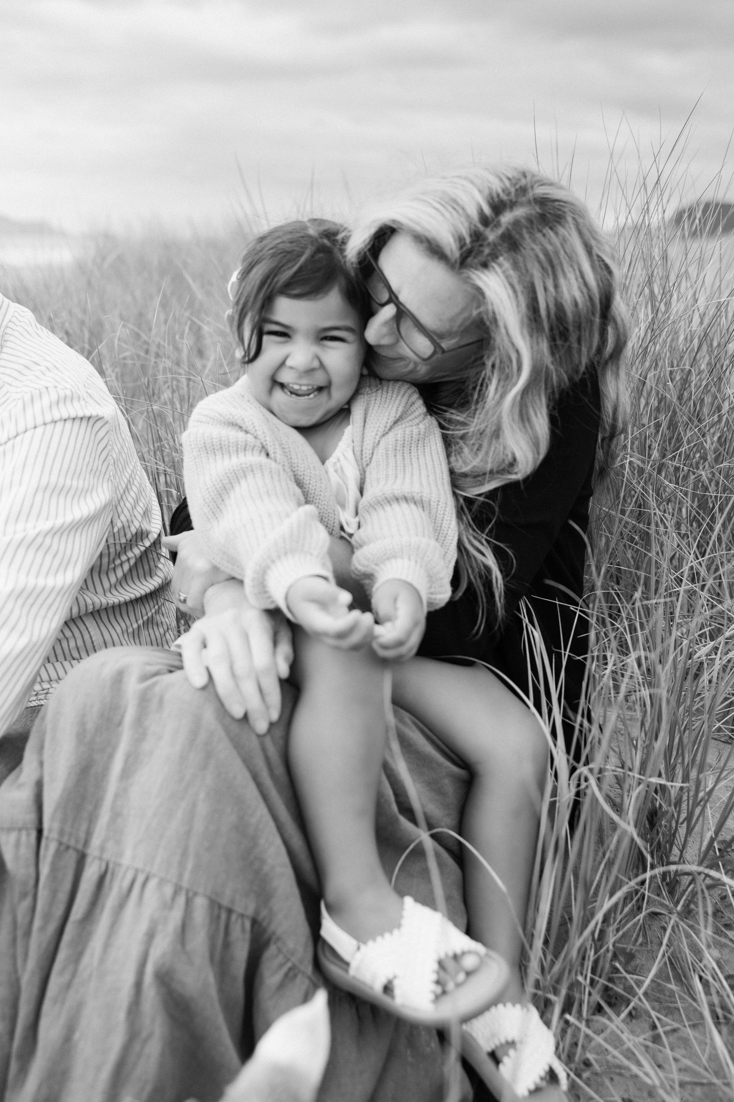Two people share a joyful moment together while sitting in tall grass on a cloudy day.