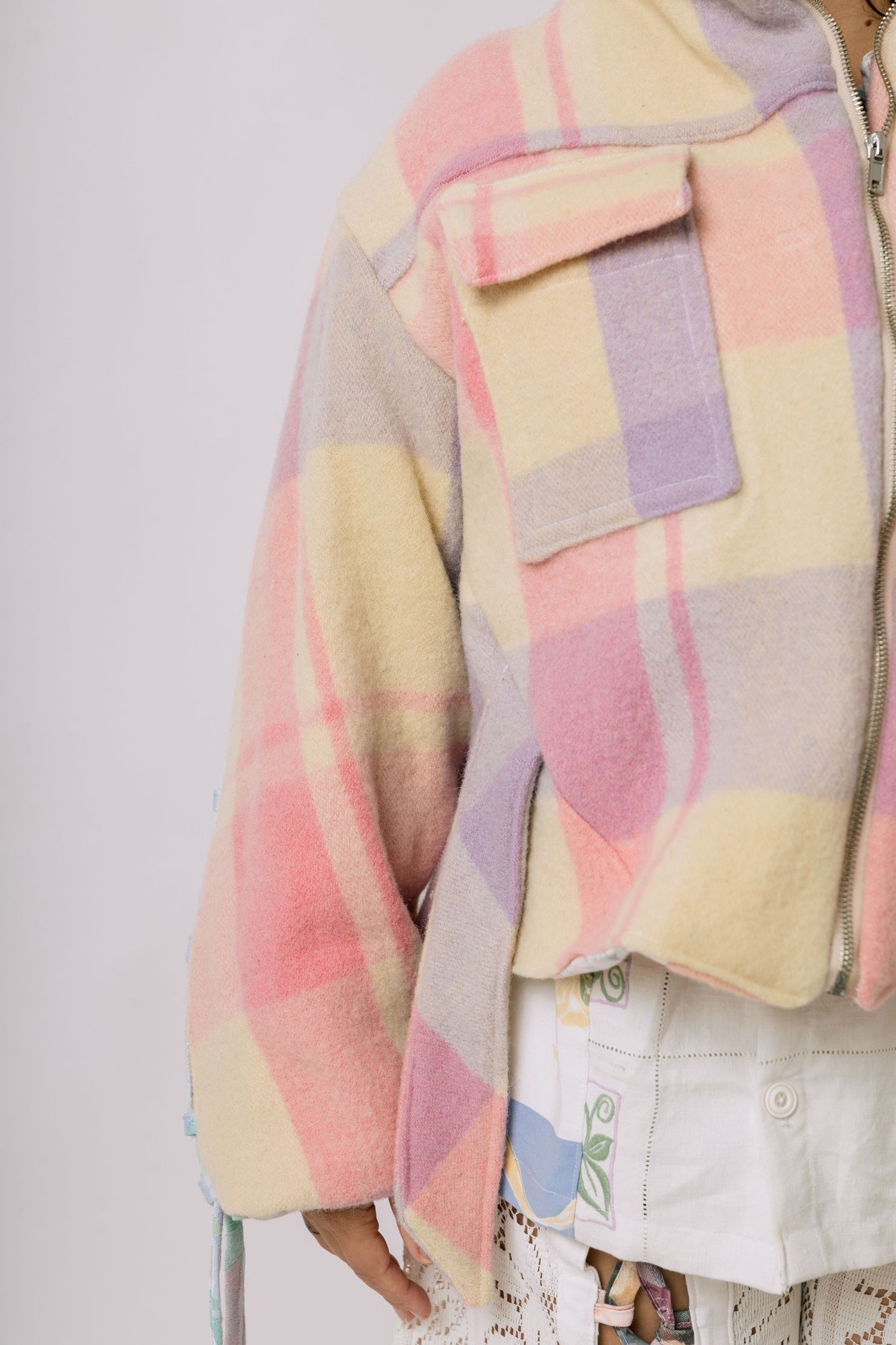 Pastel plaid fleece jacket in soft pink, yellow and purple tones with a chest pocket and zipper closure.