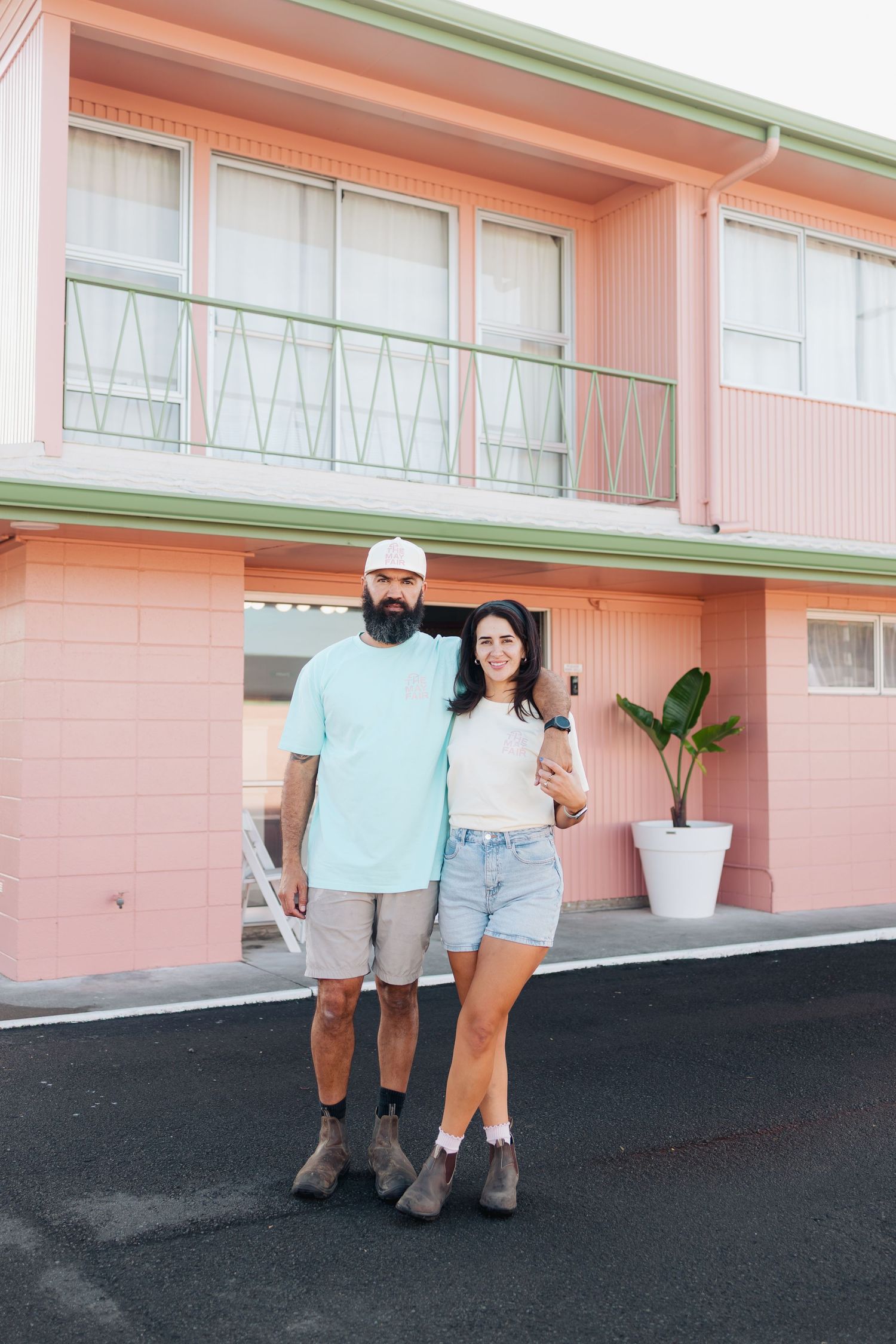 Couple standing in front of pink retro motel exterior.