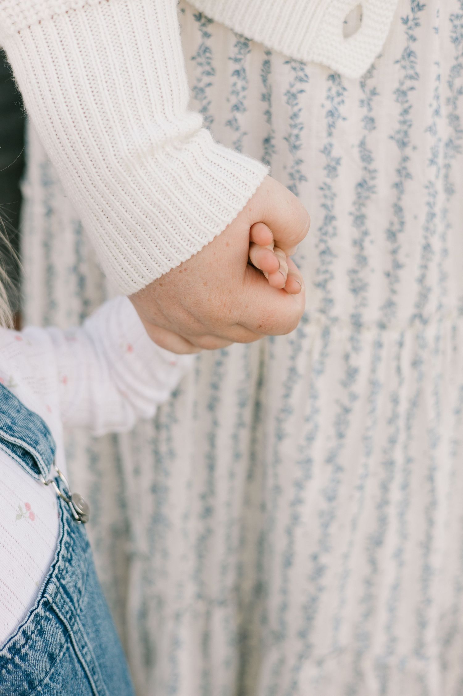 Close-up of a small hand holding onto a white knit sweater sleeve against a floral wallpaper background.