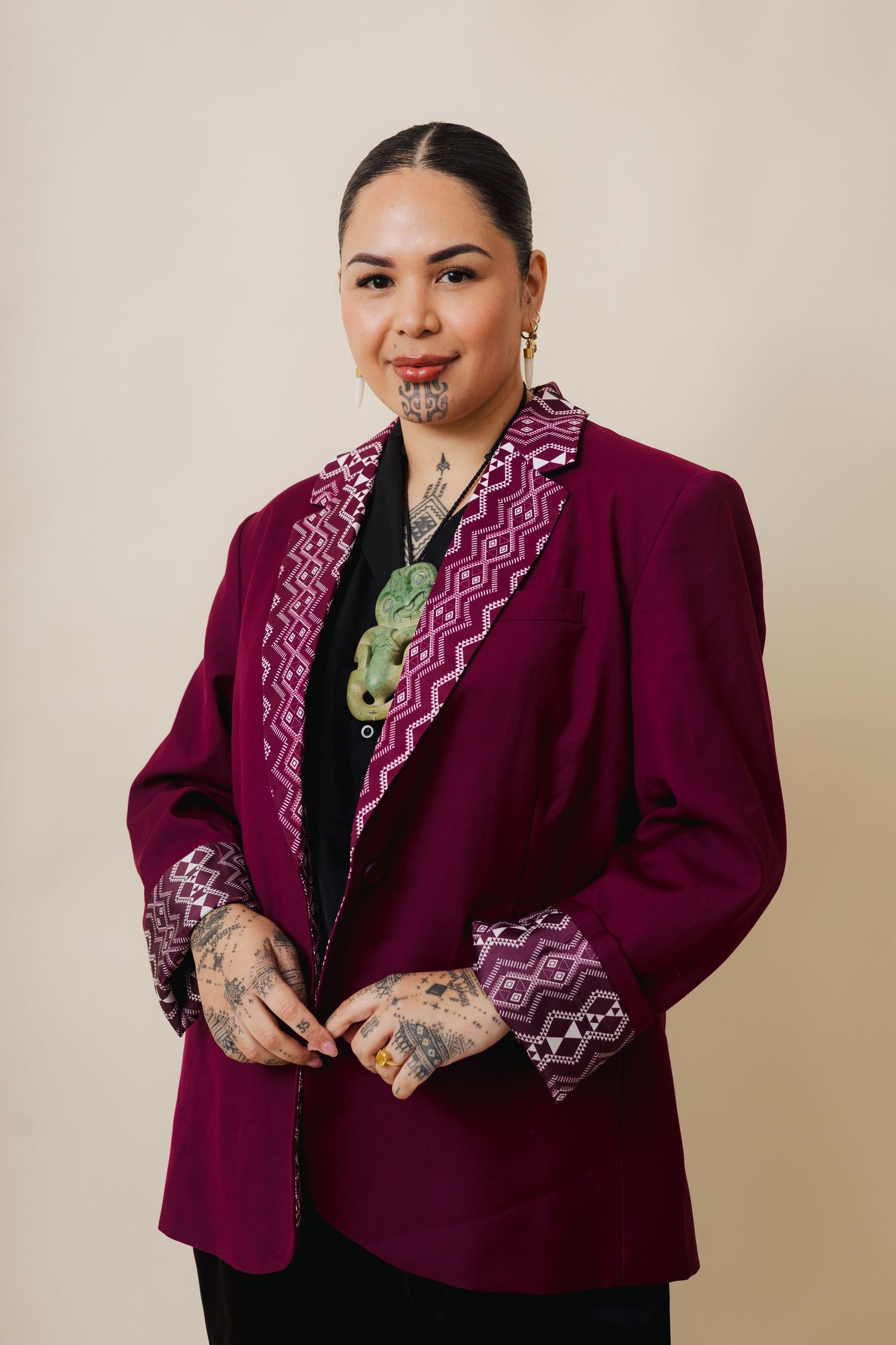 A person wearing a burgundy blazer with white zigzag trim poses in different angles against a beige background.