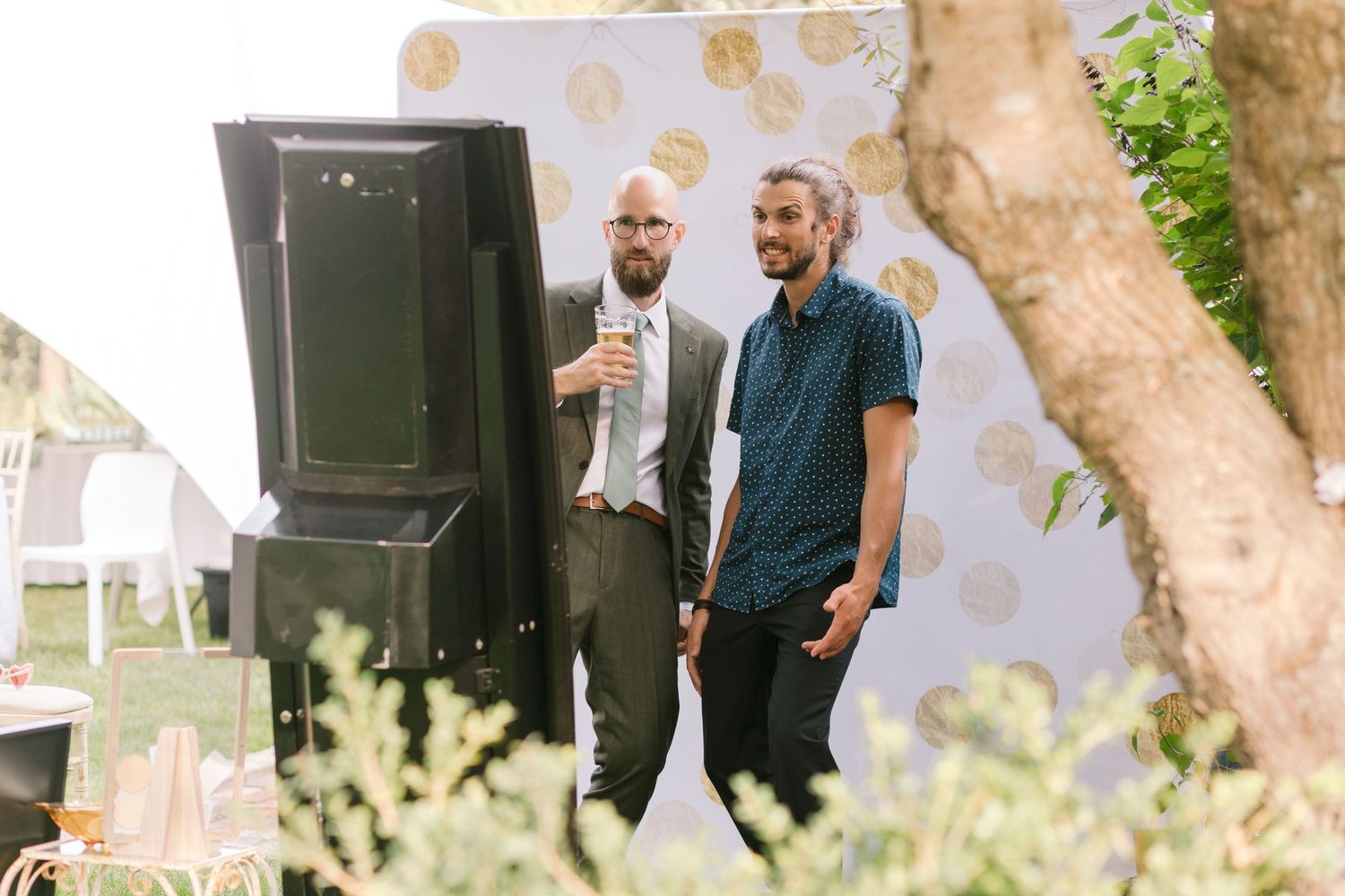 Wedding celebration with guests gathered under outdoor trees with lighting and speakers.