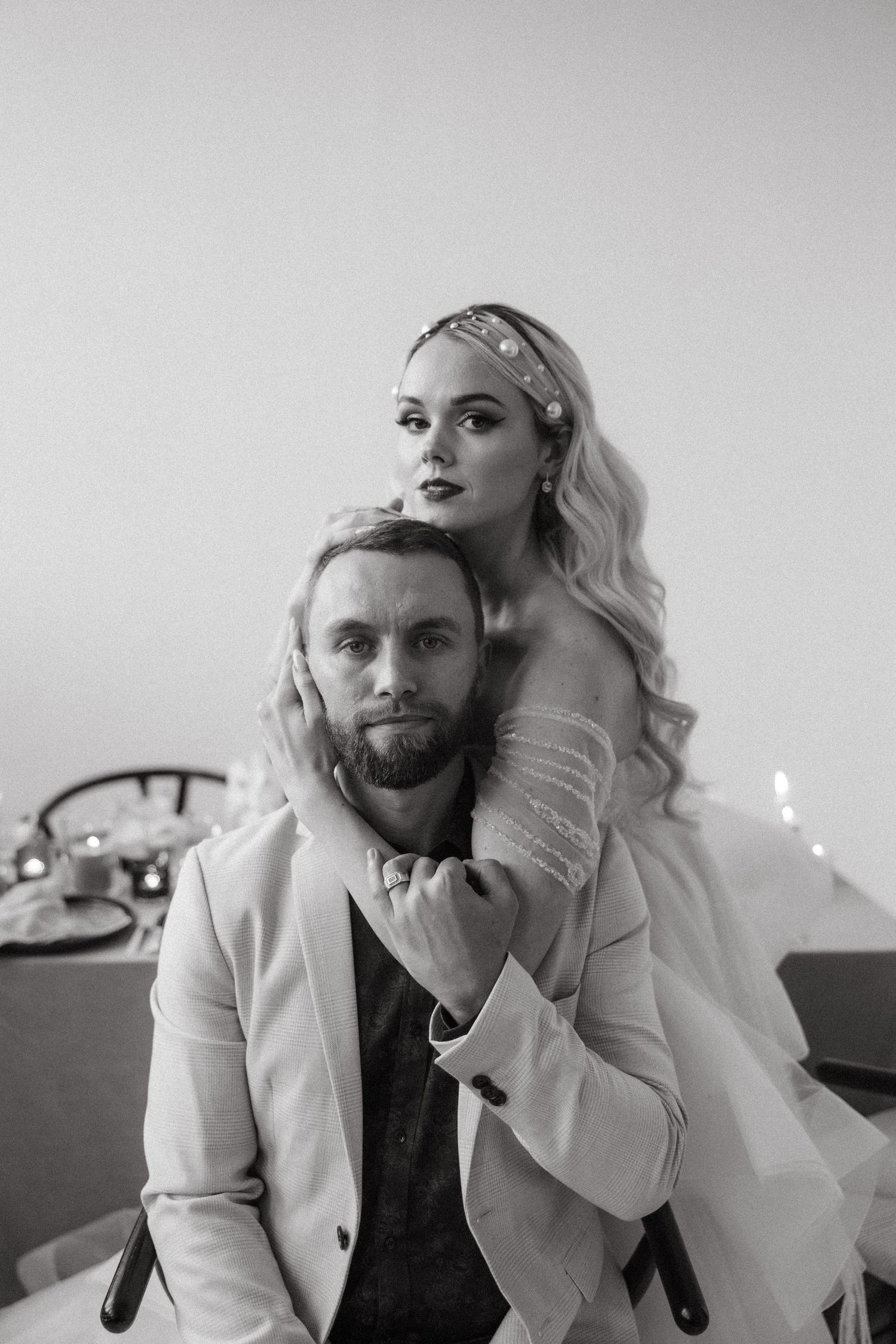 Romantic black and white portrait of couple in elegant attire with woman embracing man from behind in intimate pose.
