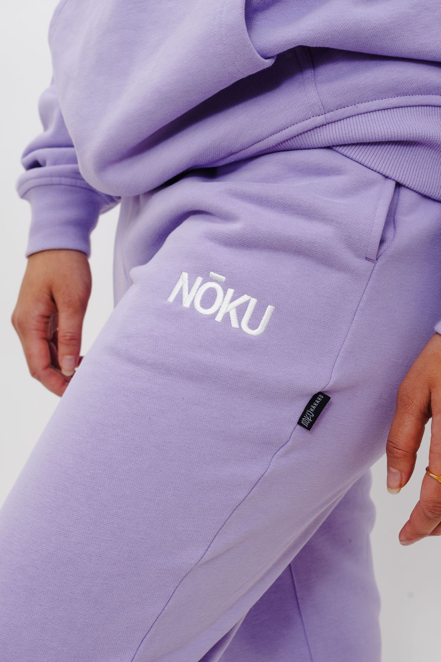 Close-up of lavender sweatpants with white NOKU logo and pocket detail shown against white background.