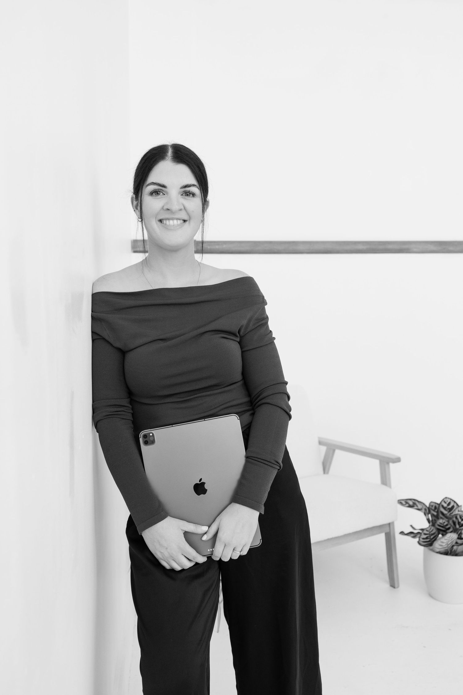 Professional studio portraits show a person in a black off-shoulder dress holding an Apple laptop against a white background.