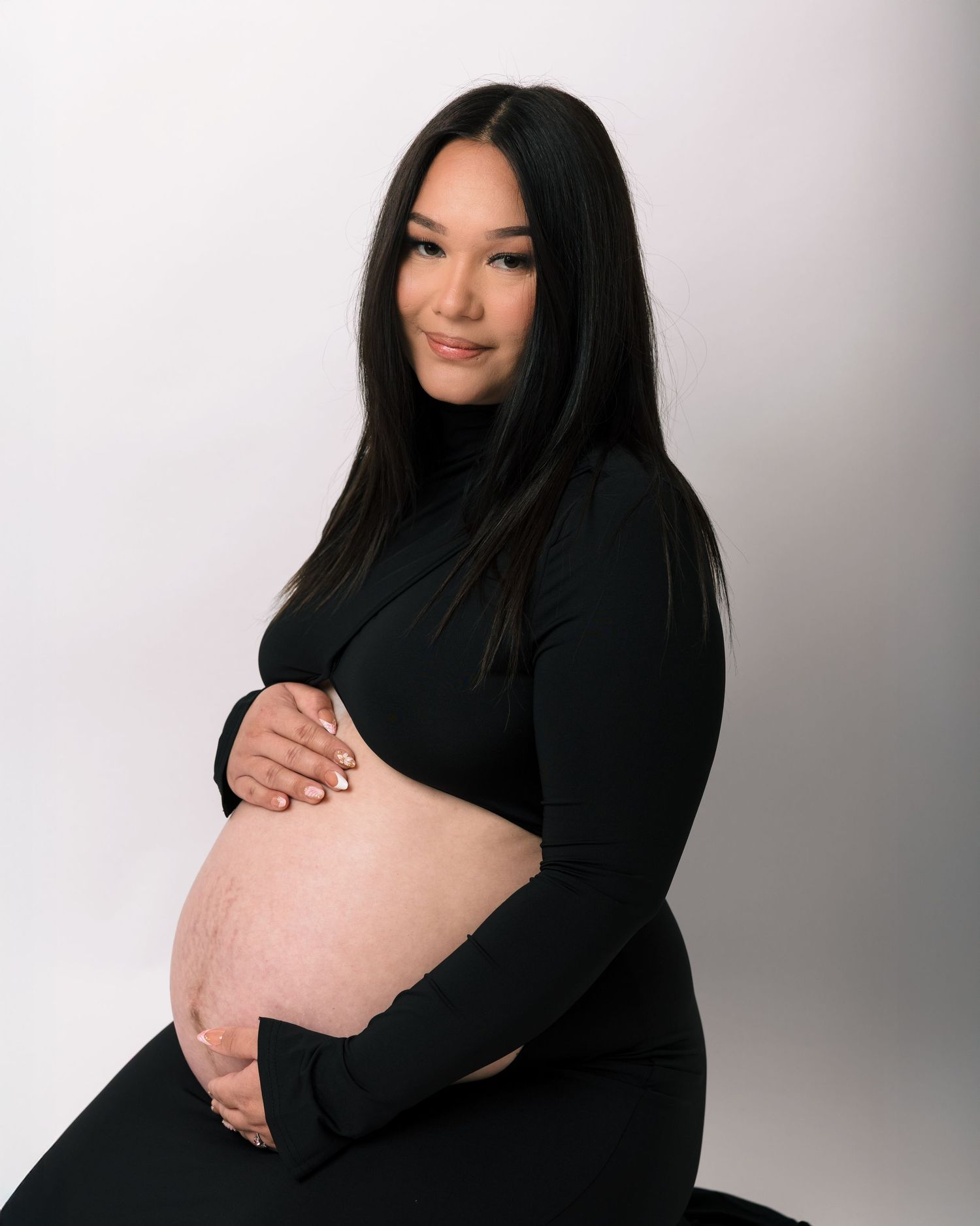 A pregnant woman in a black outfit cradling her bare baby bump during a maternity photoshoot.