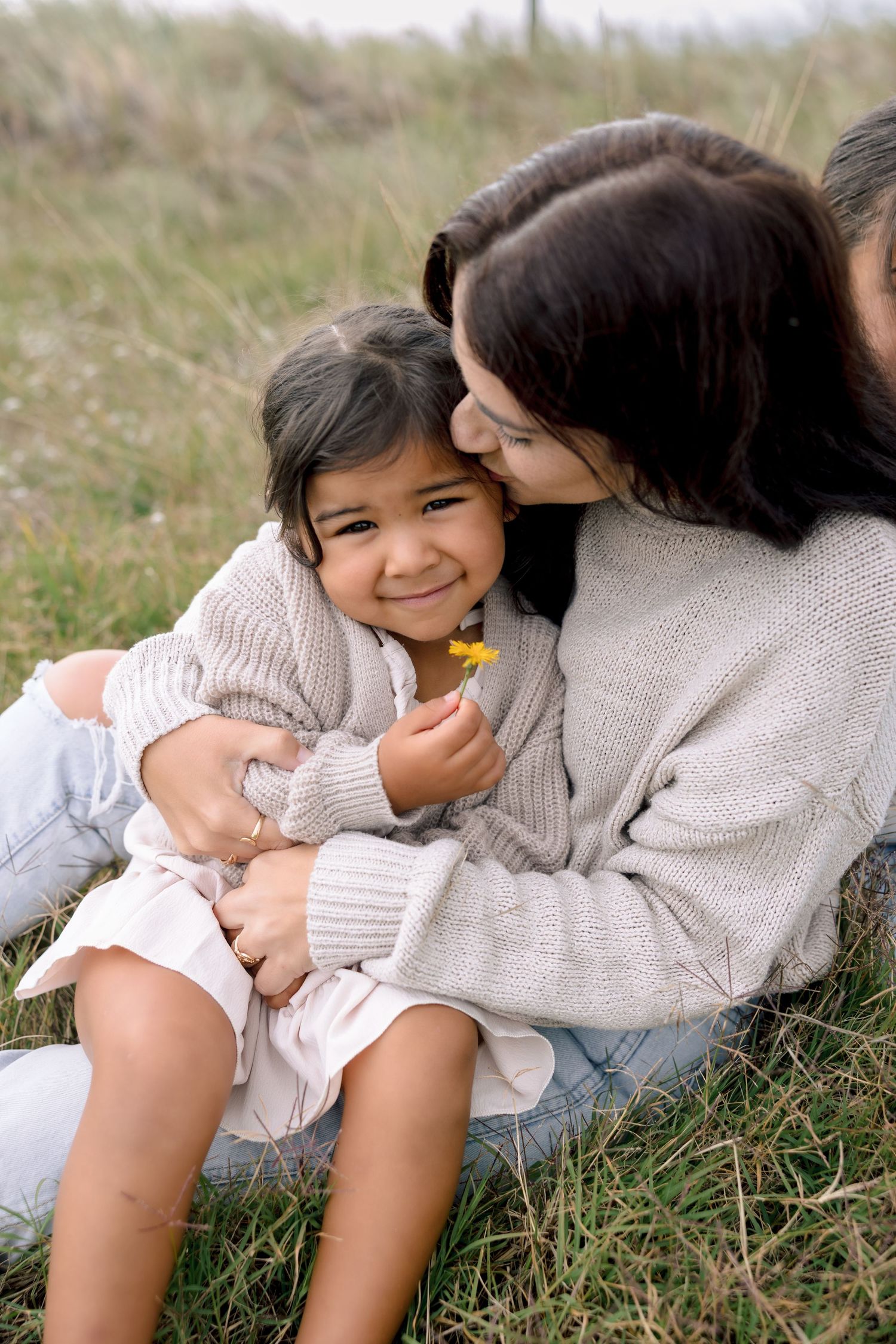 A tender moment shared between parent and child lying in grass during a sunny outdoor photo session.