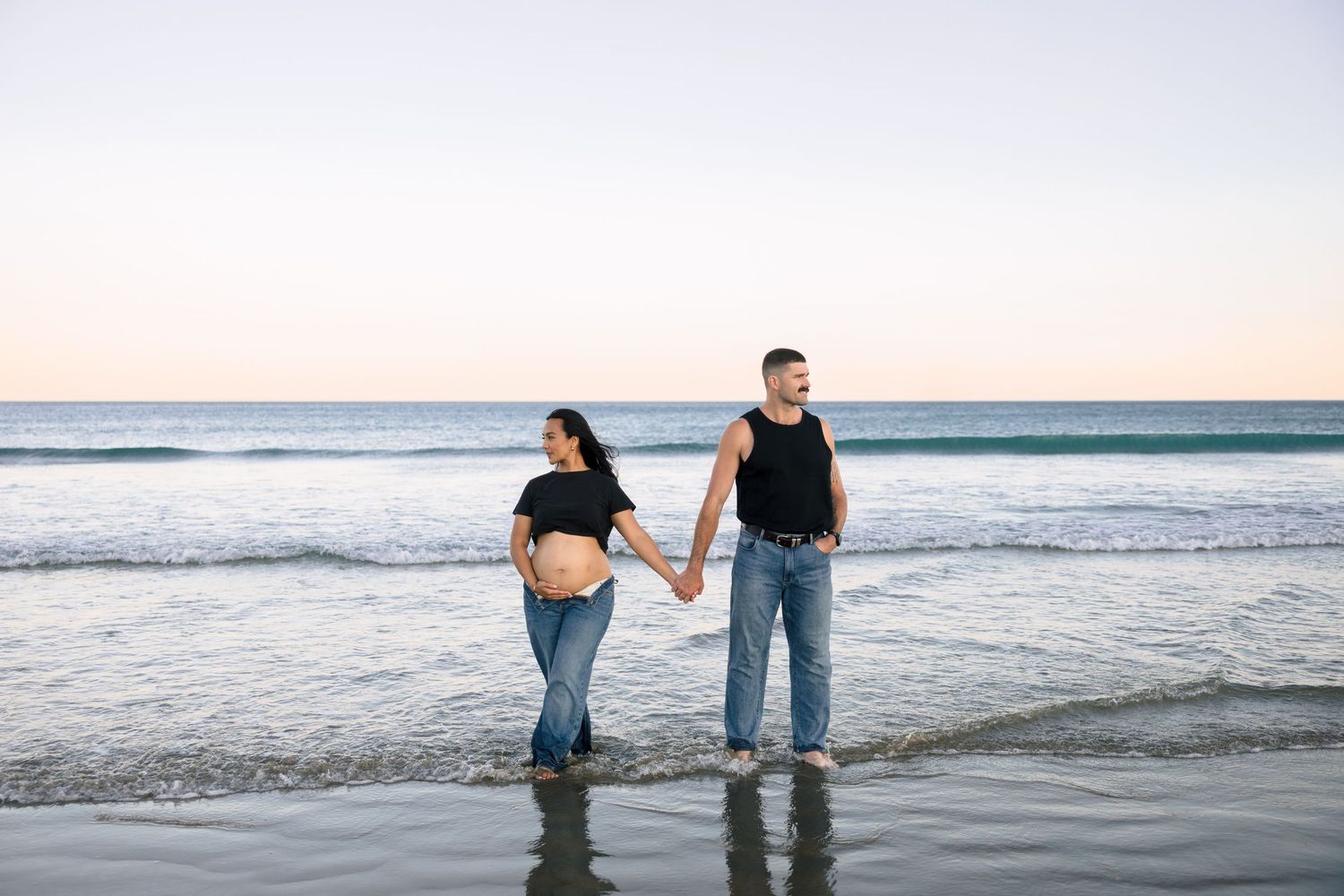 Two people walk together along the shoreline at sunset as ocean waves roll onto the sandy beach.
