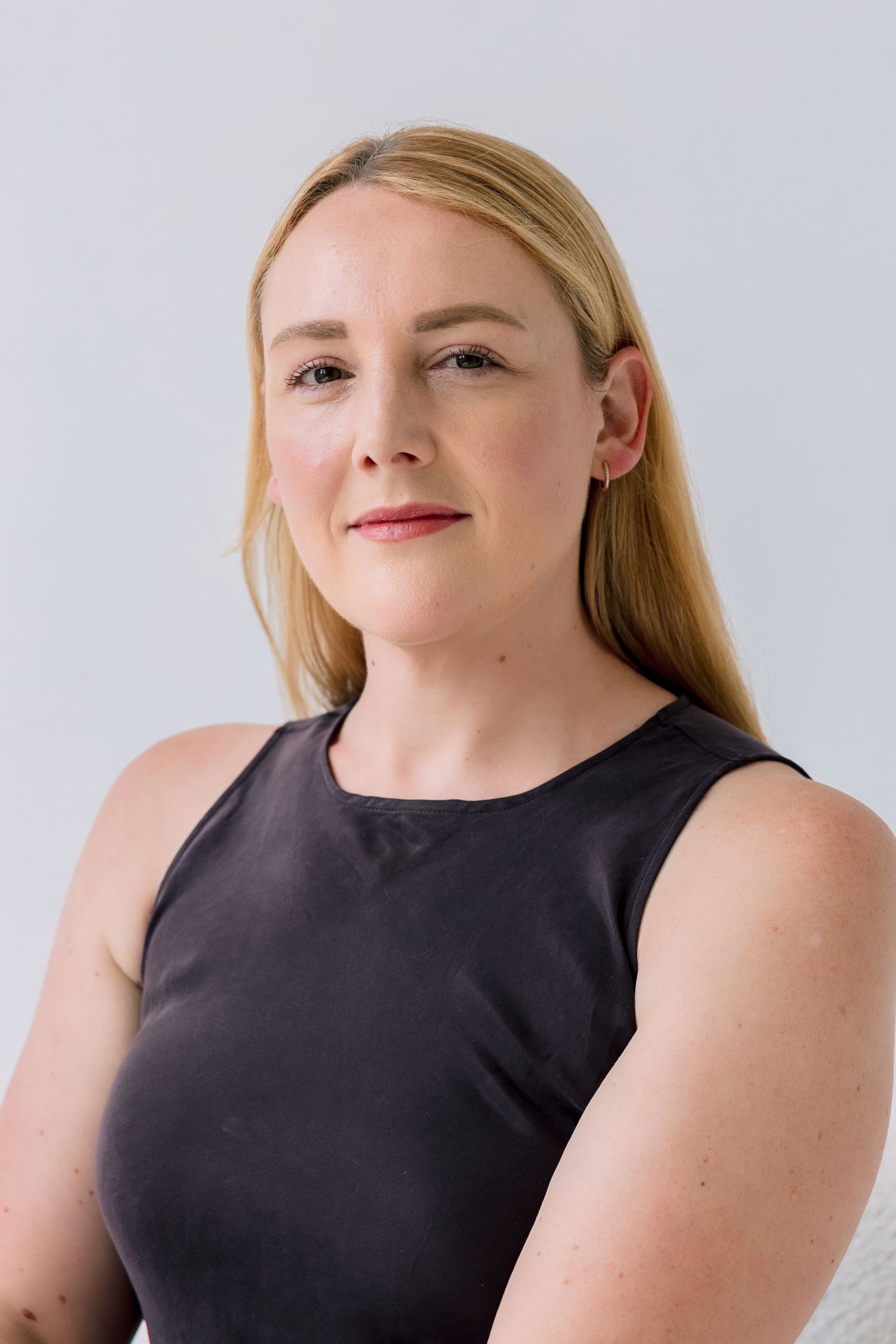A person with blonde hair wearing a black sleeveless top poses against a light background in a series of headshots.