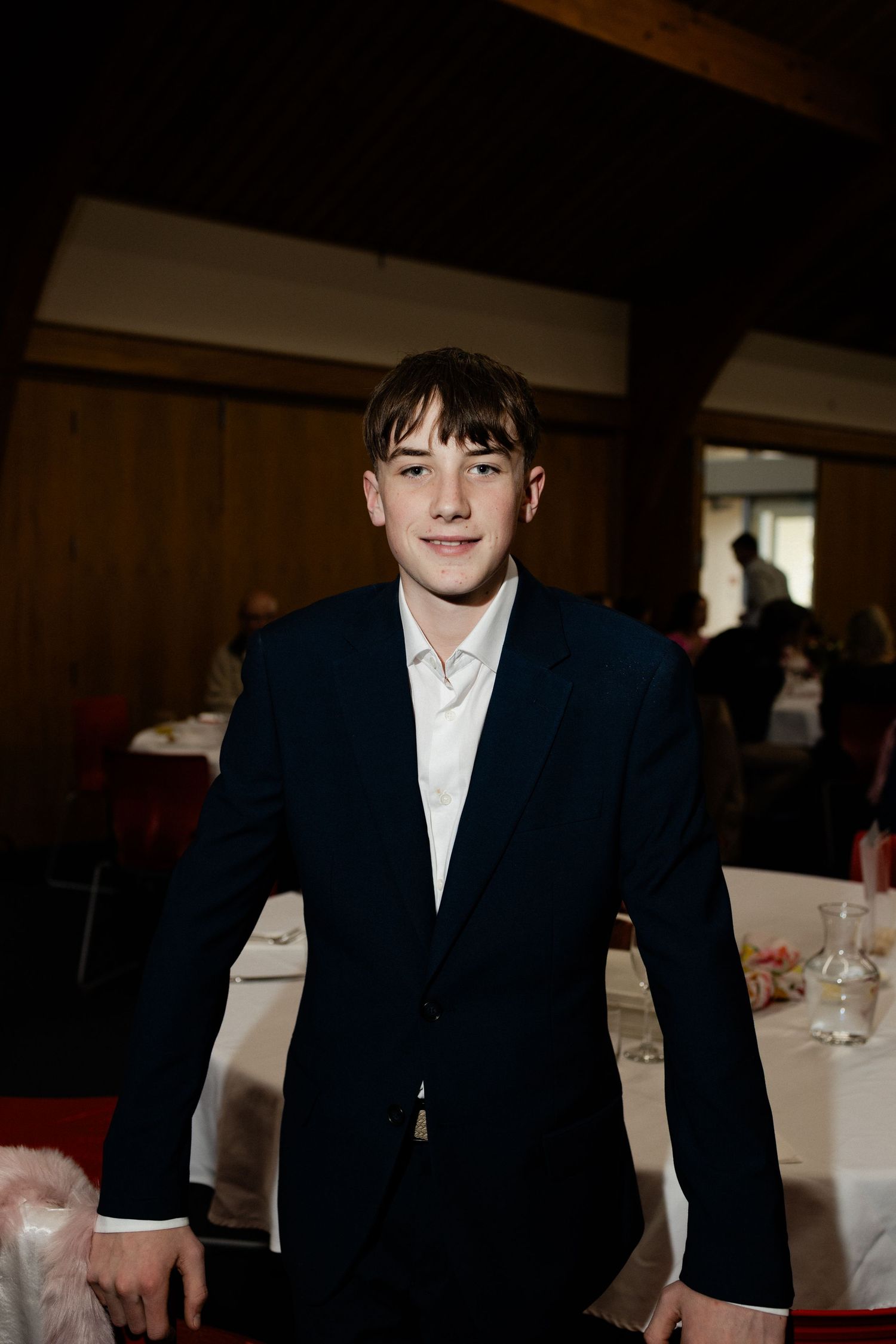 A person in formal attire sits at a table in a dimly lit banquet hall.
