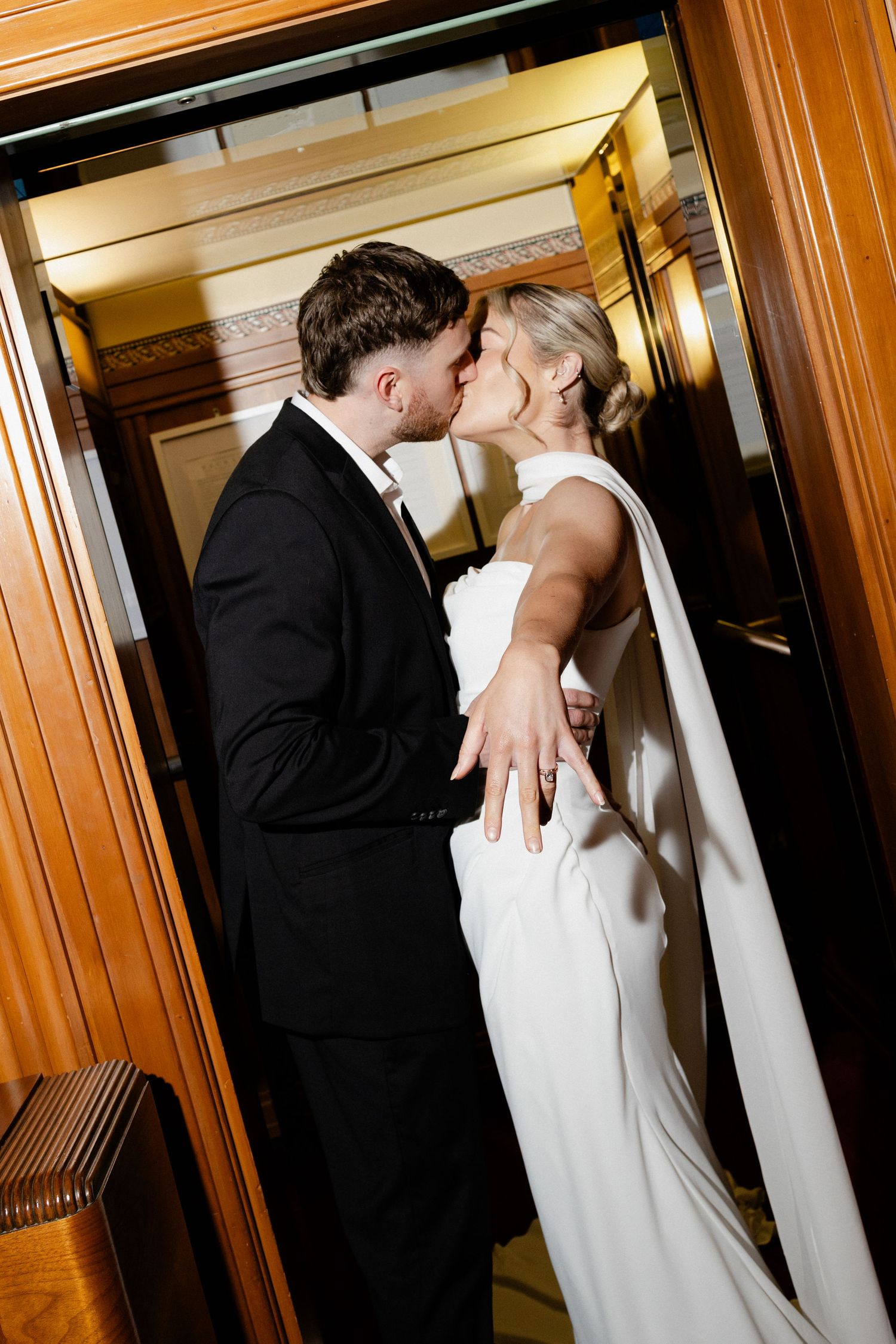 A romantic wedding couple shares intimate moments in a wood-paneled hallway with warm lighting.
