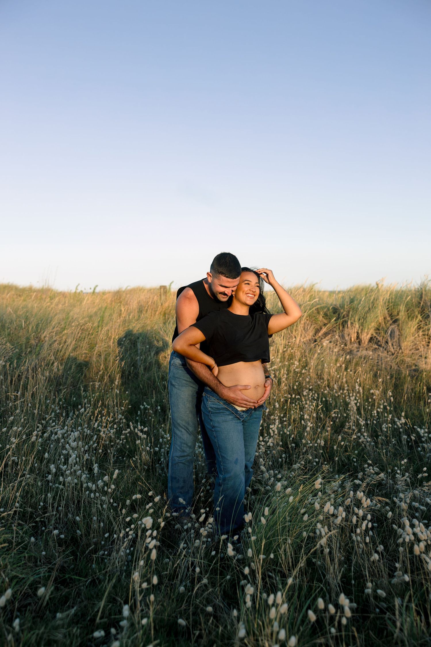 Couple embracing in a sunlit meadow of tall wildflowers during golden hour.