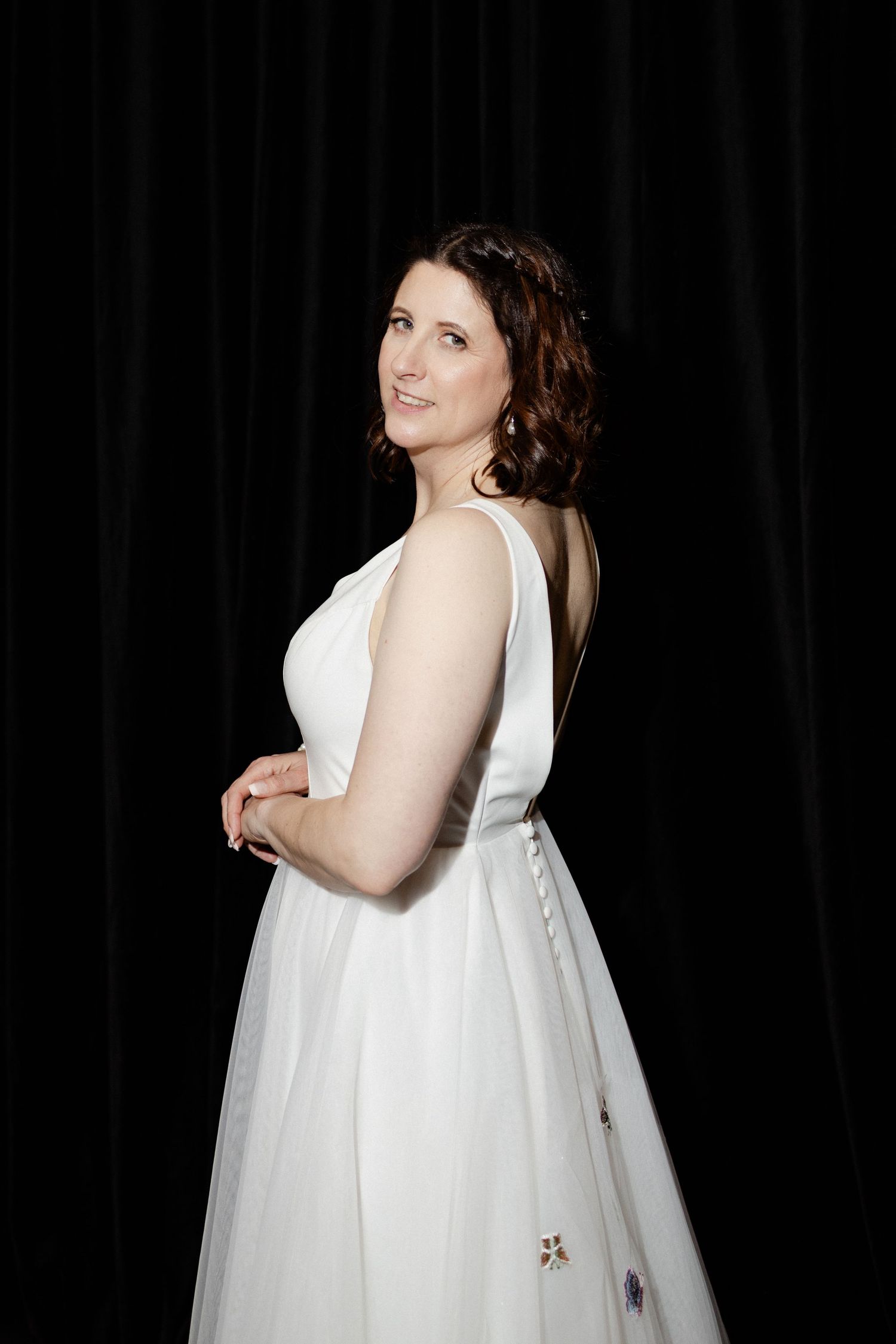 A woman in an elegant white sleeveless dress poses against a dark background during a formal portrait session.