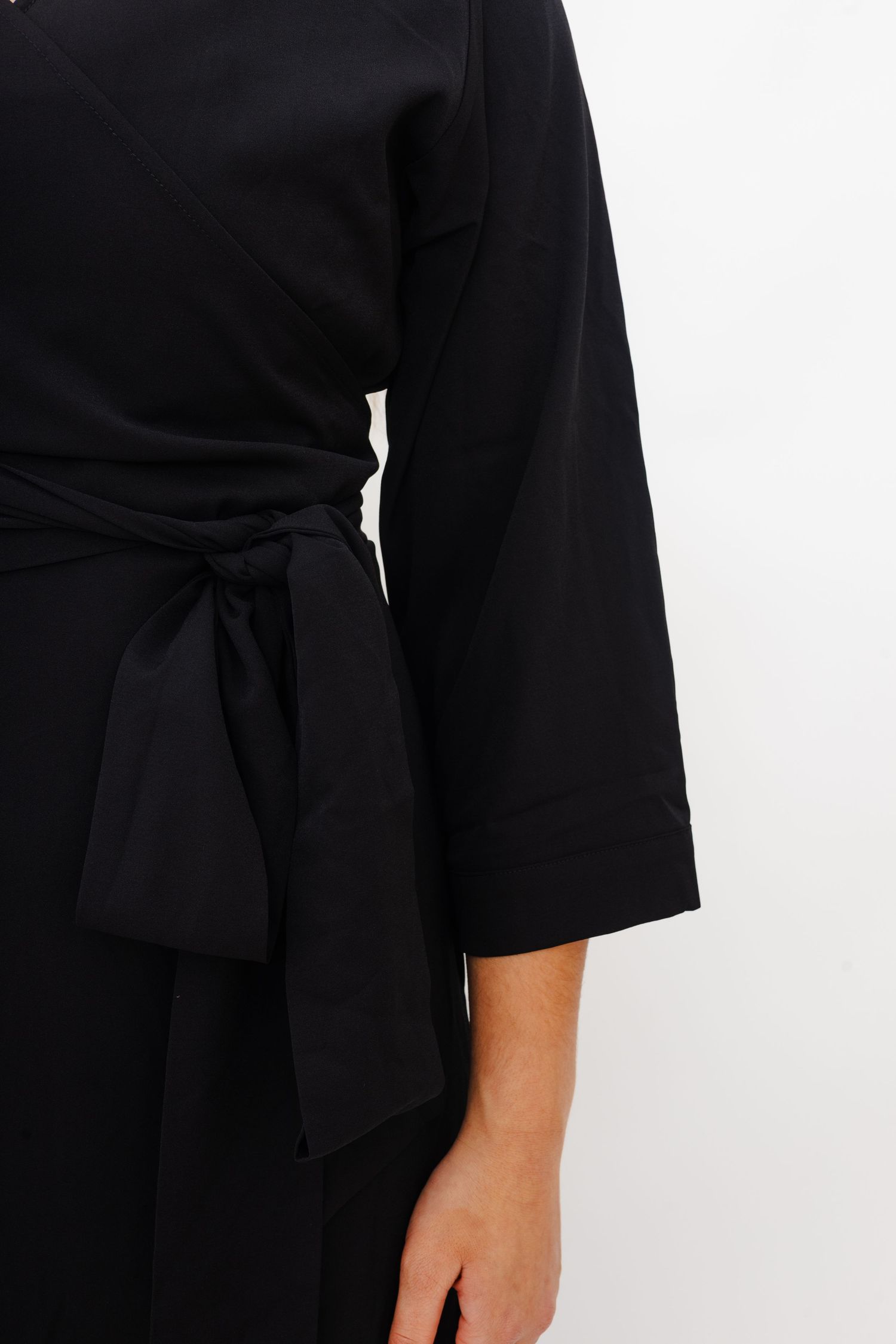 Detail of a black wrap dress with three-quarter length sleeves and waist tie belt against white background.