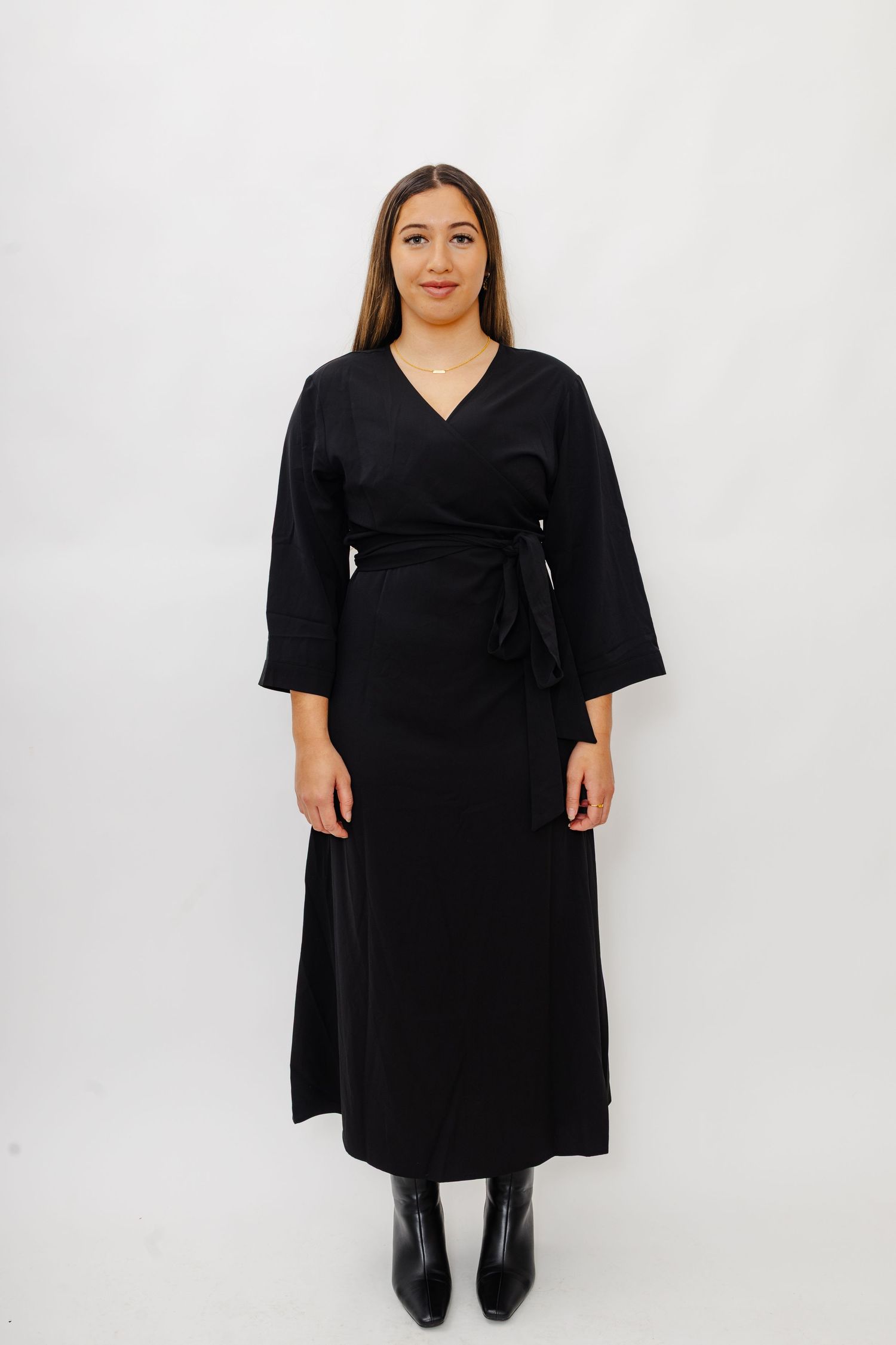 Classic black wrap midi dress with kimono sleeves, waist tie, and paired with black ankle boots against white backdrop.