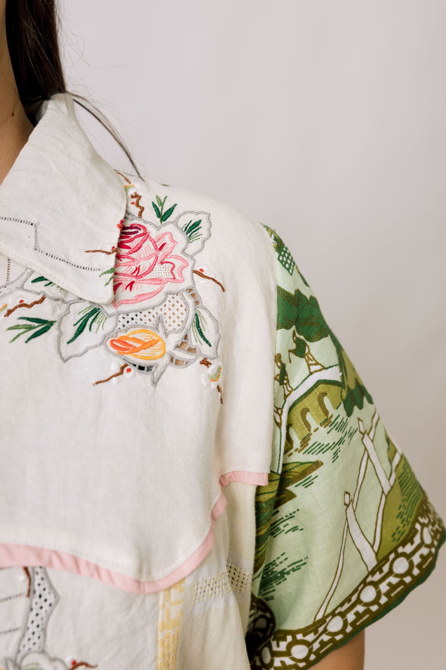 Close-up details of delicate floral embroidery on white fabric with pink and green botanical motifs.
