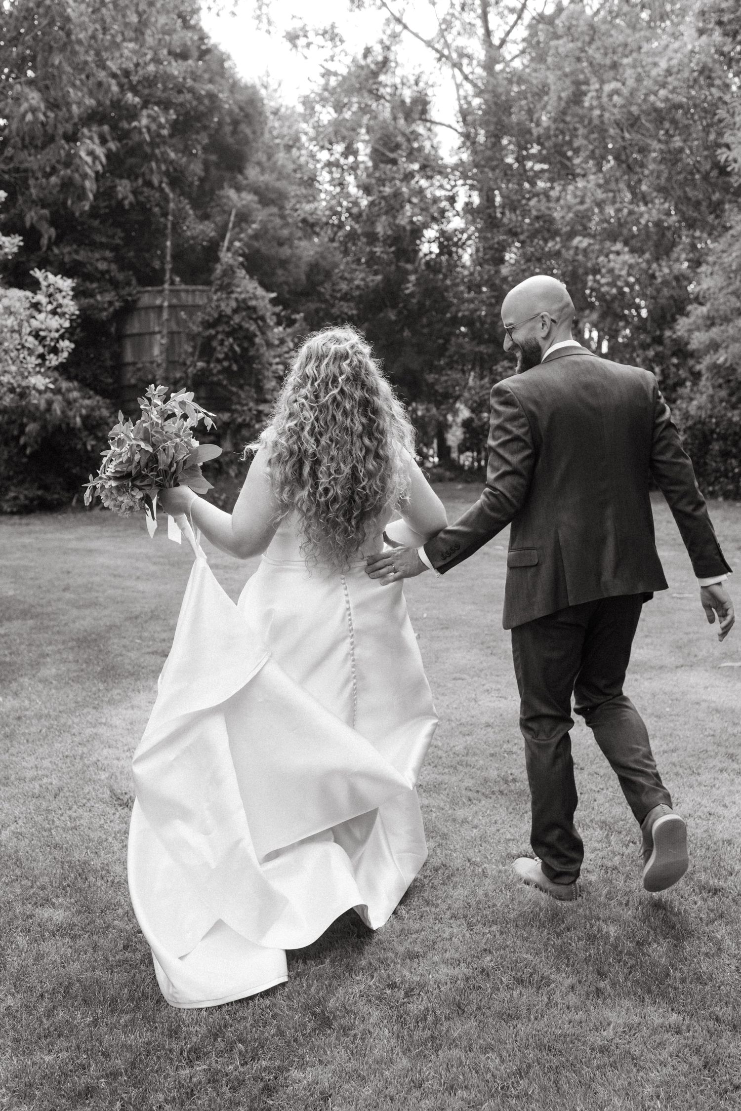 A black and white sequence of a bride and groom walking together on grass with her dress flowing in the breeze.