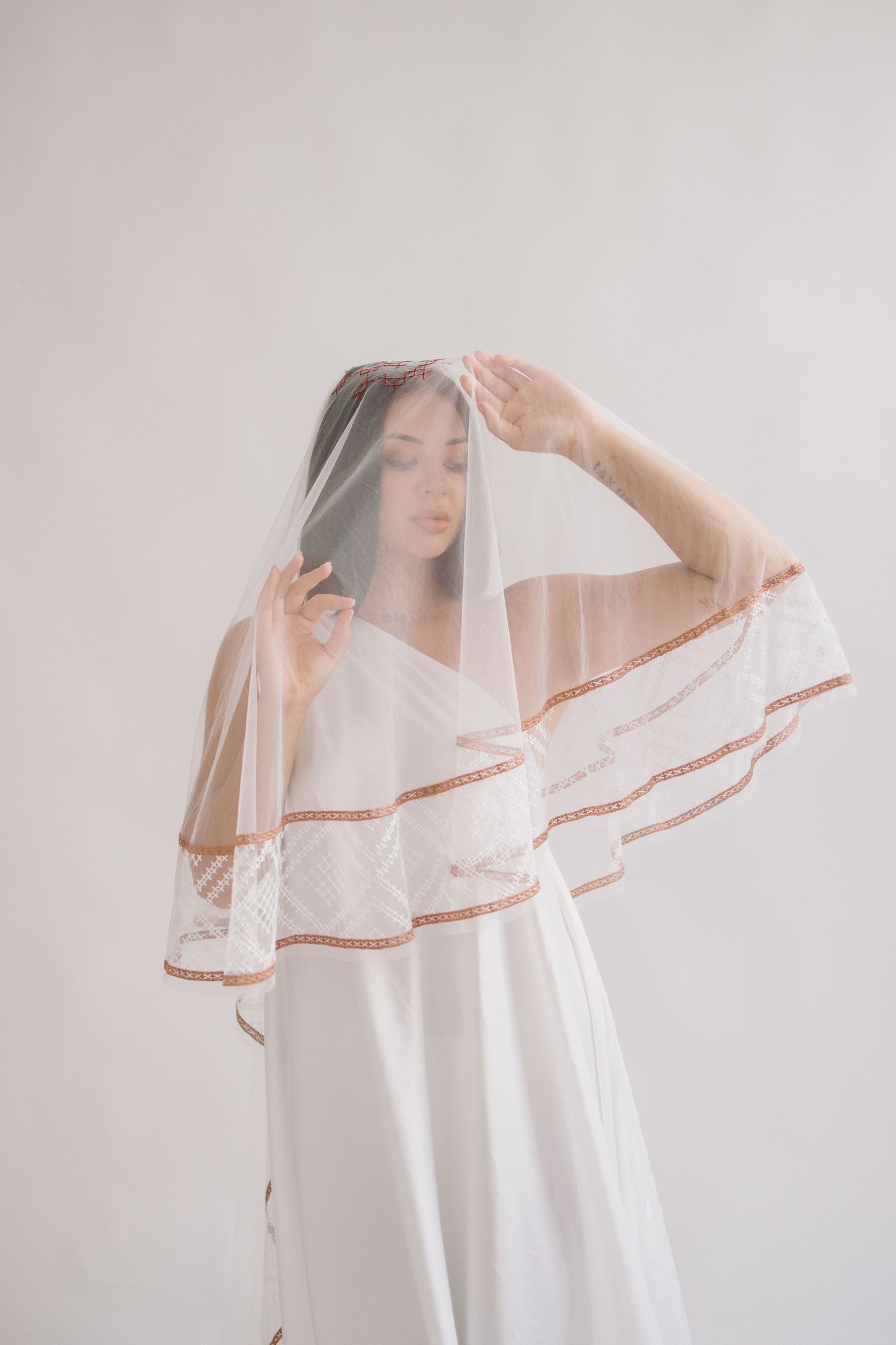Ethereal bridal portrait featuring flowing white dress and delicate veil with lace trim details in minimalist setting.