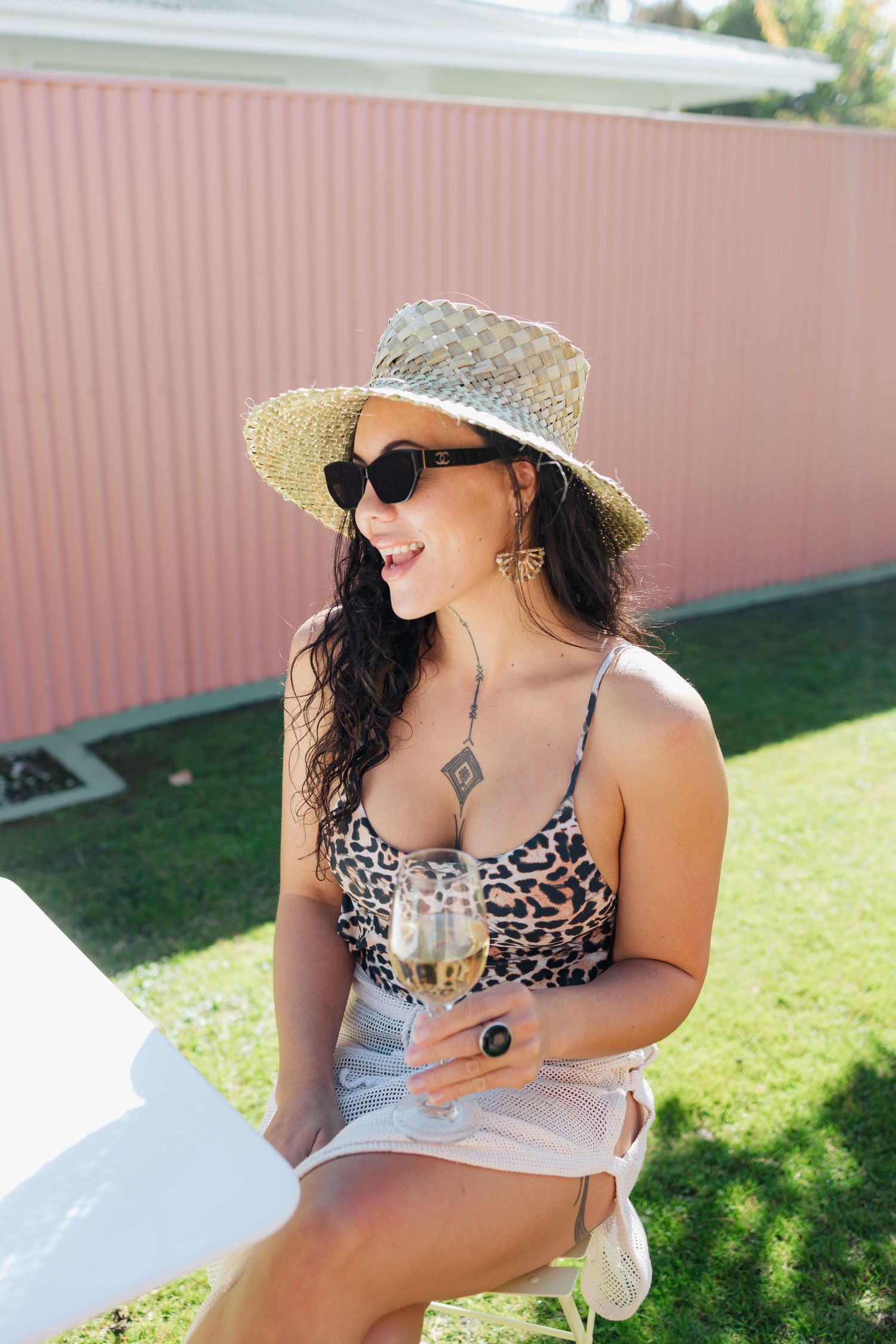 Summer outdoor scene with wine glass and straw hat against pink wall.