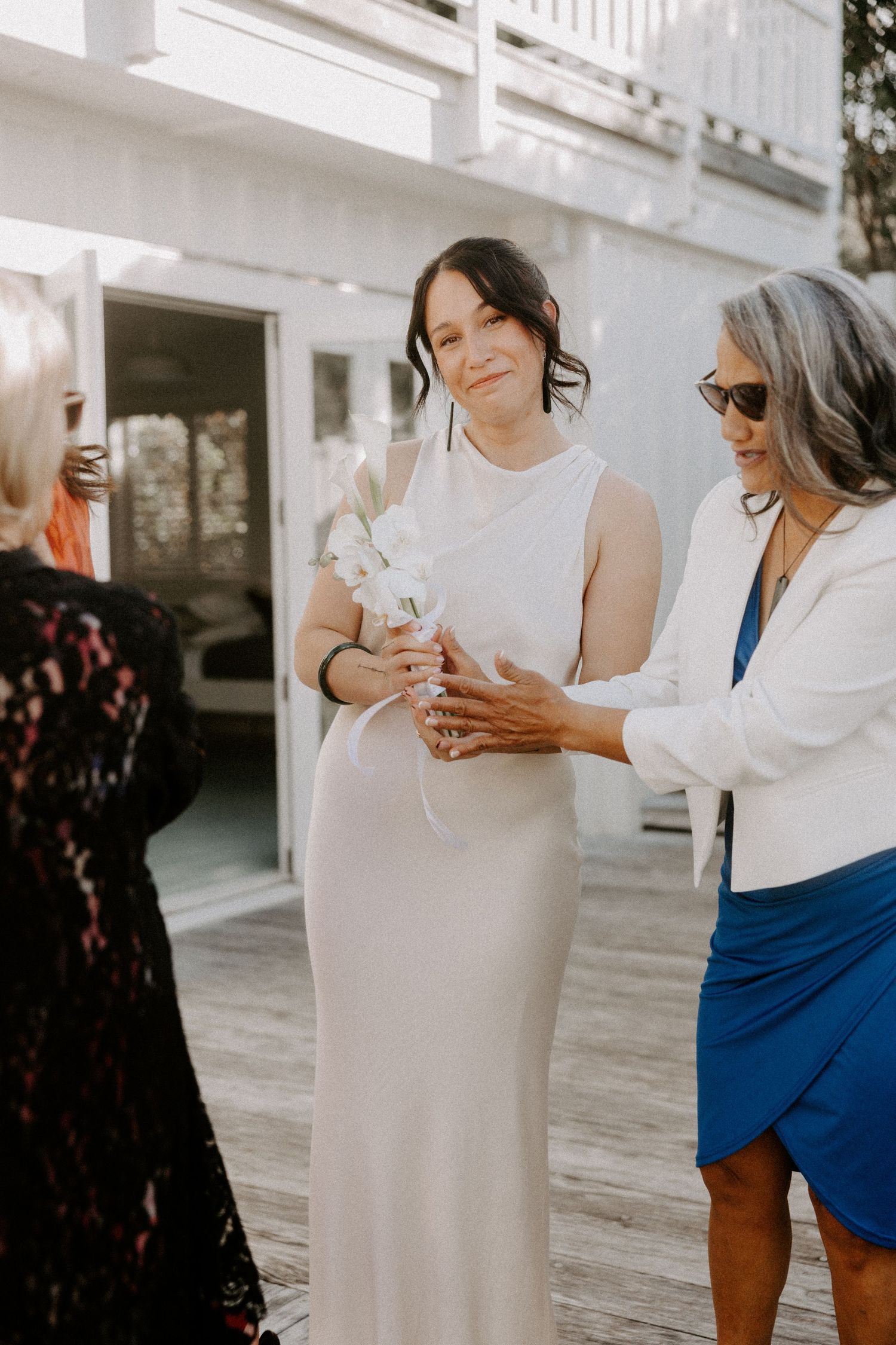 Elegant wedding scene on a white porch with guests in a mix of formal attire including black lace and blue dresses.