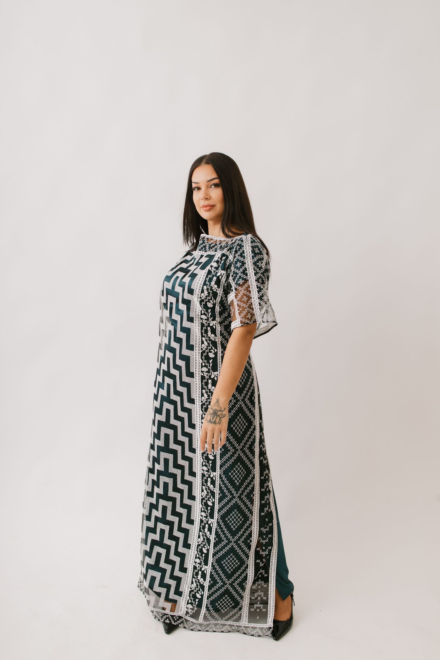 A person stands in a flowing black and white patterned maxi dress with geometric designs against a light background.