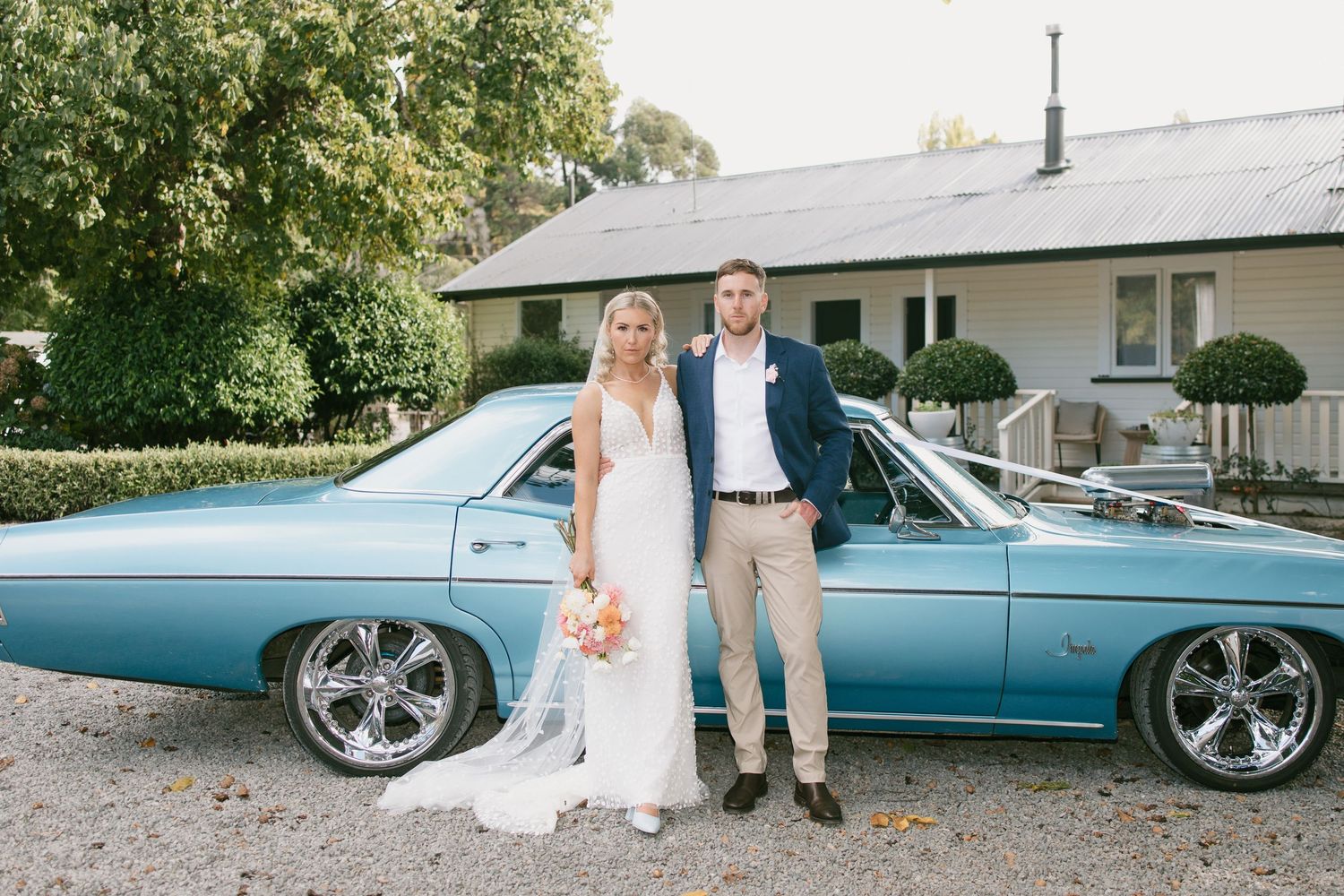 A couple stands next to a classic light blue car on their wedding day.