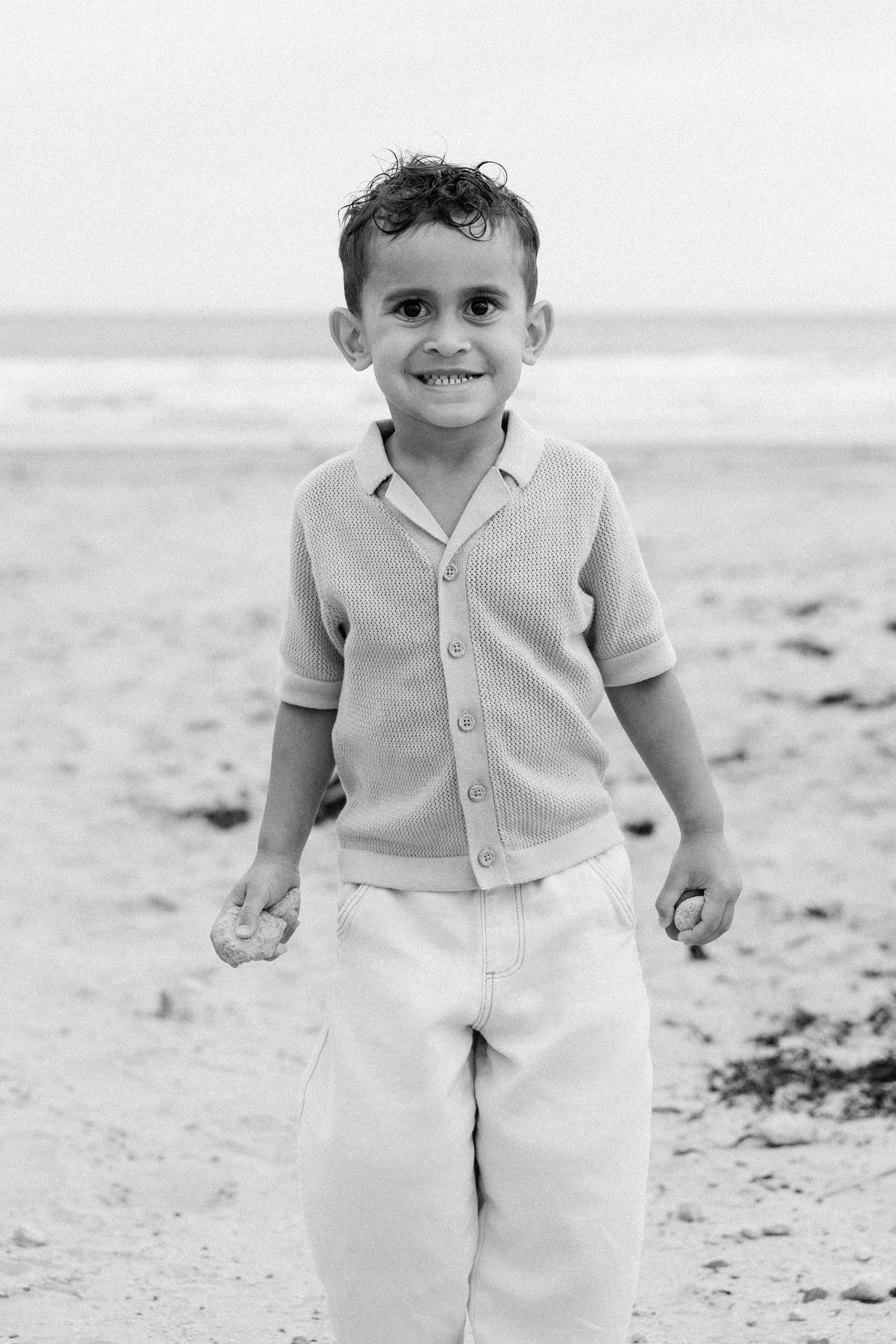 Black and white photo series of a child in white pants and cardigan playing on a sandy beach.