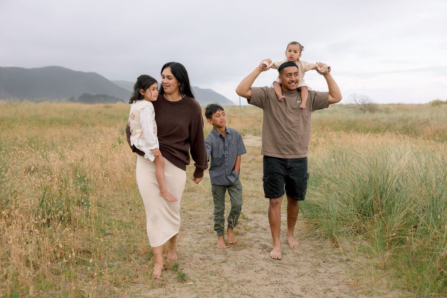 A family walks together through a grassy meadow on a sunny summer day, captured in a series of candid moments.
